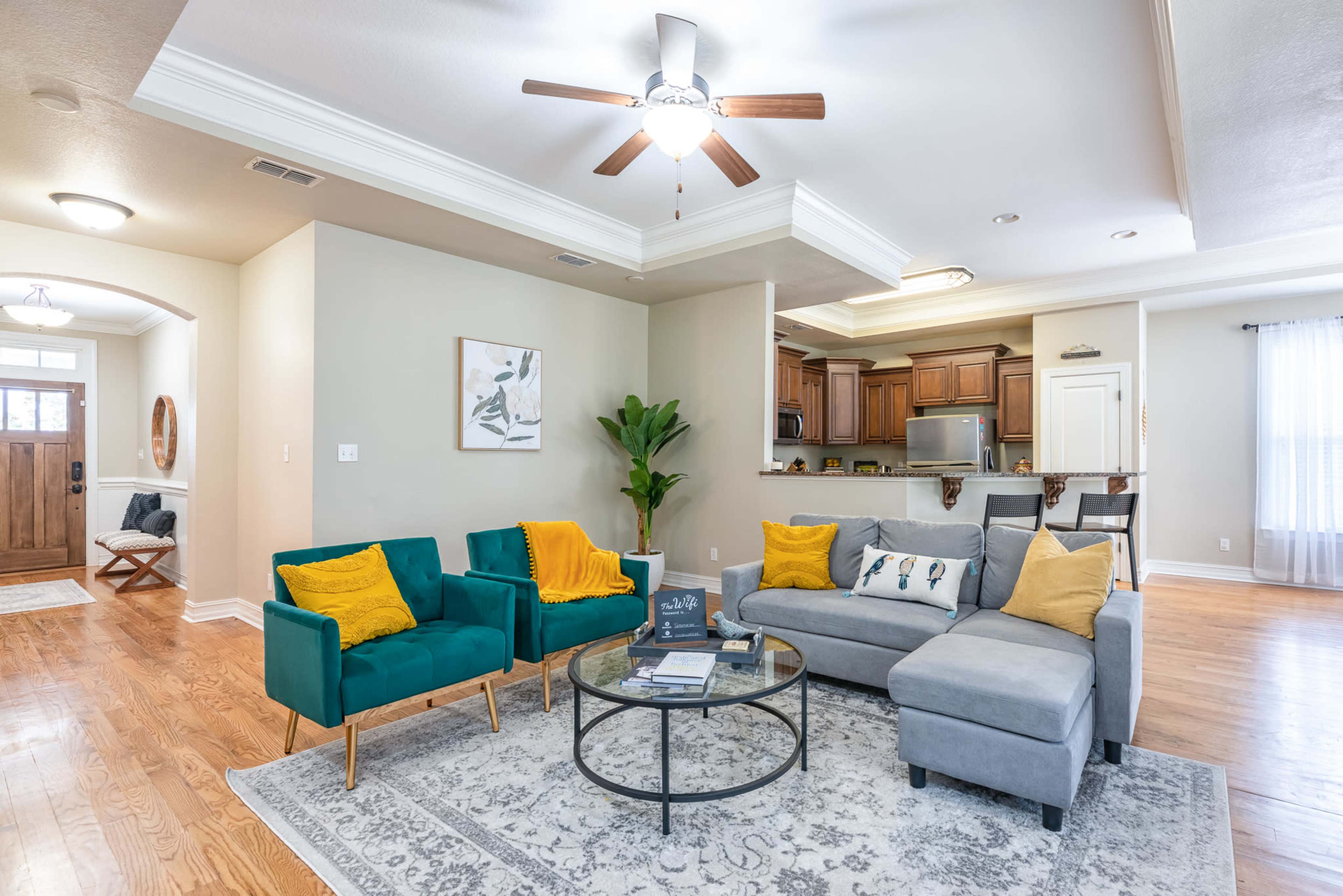The living room features a sectional sofa, two upholstered chairs, a round coffee table, and a clear view of a kitchen area in the background.