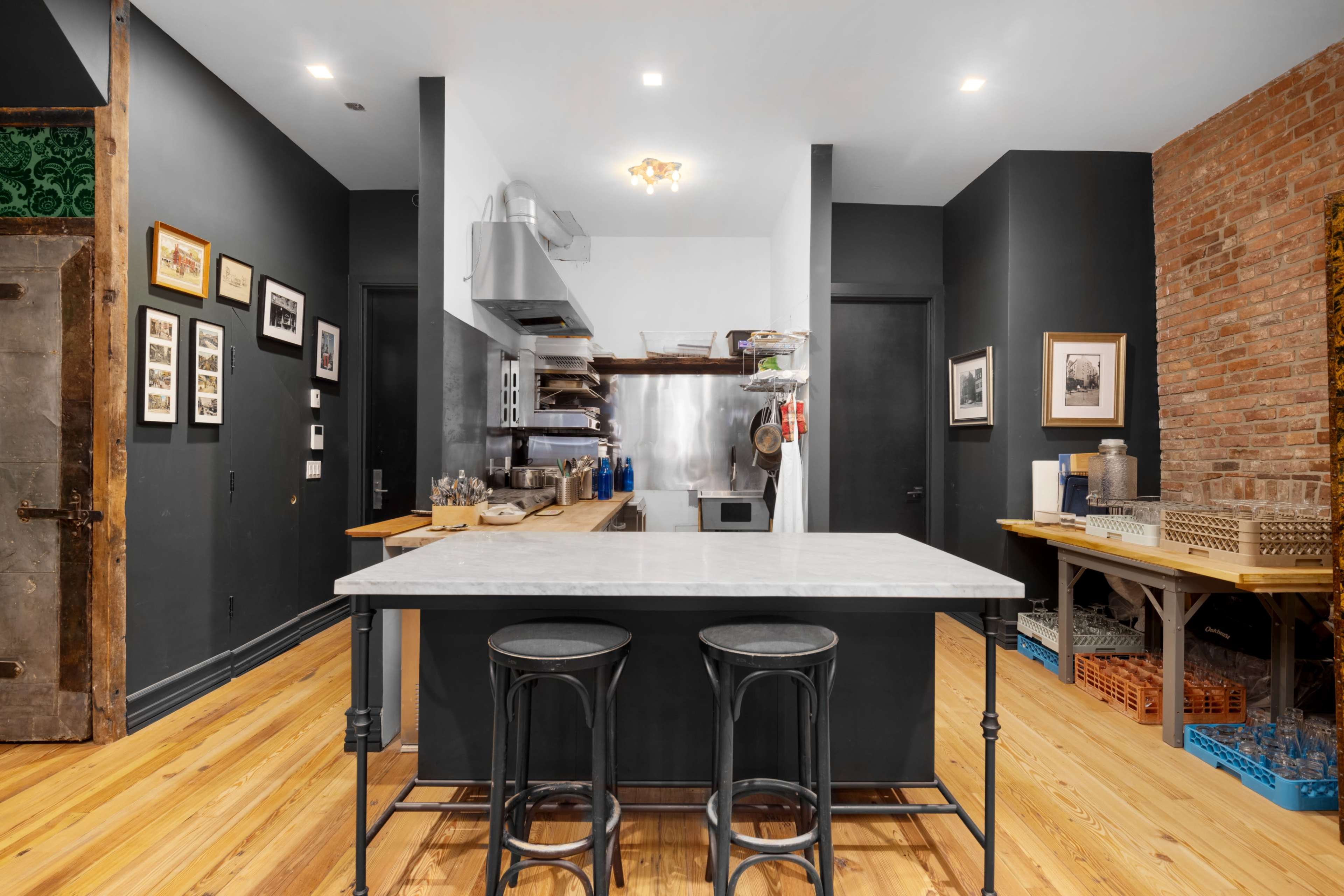 A modern kitchen with a marble island, stainless steel appliances, and exposed brick walls.