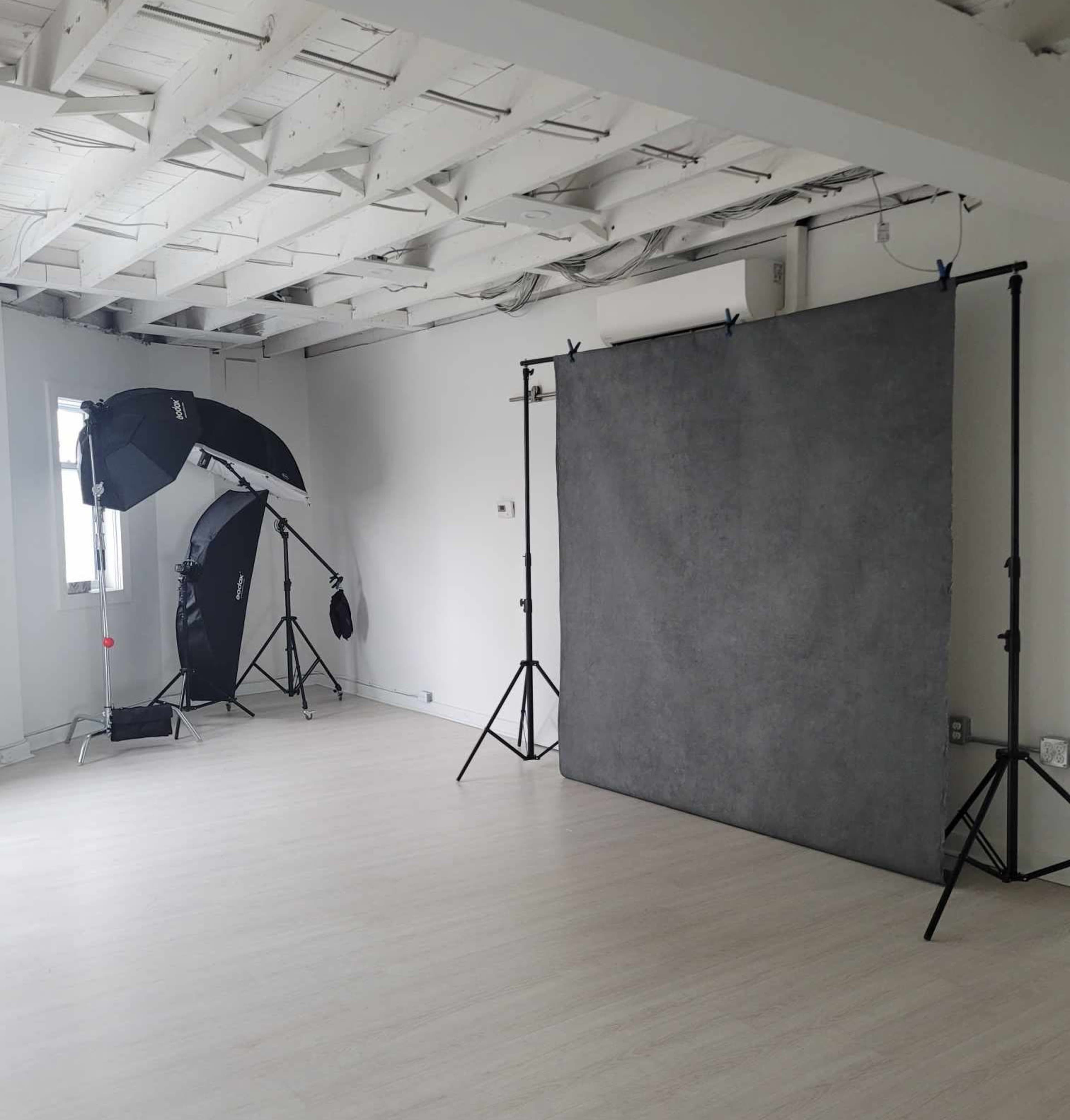 A photography studio with a gray backdrop on a support frame and two softbox lights positioned on tripods.