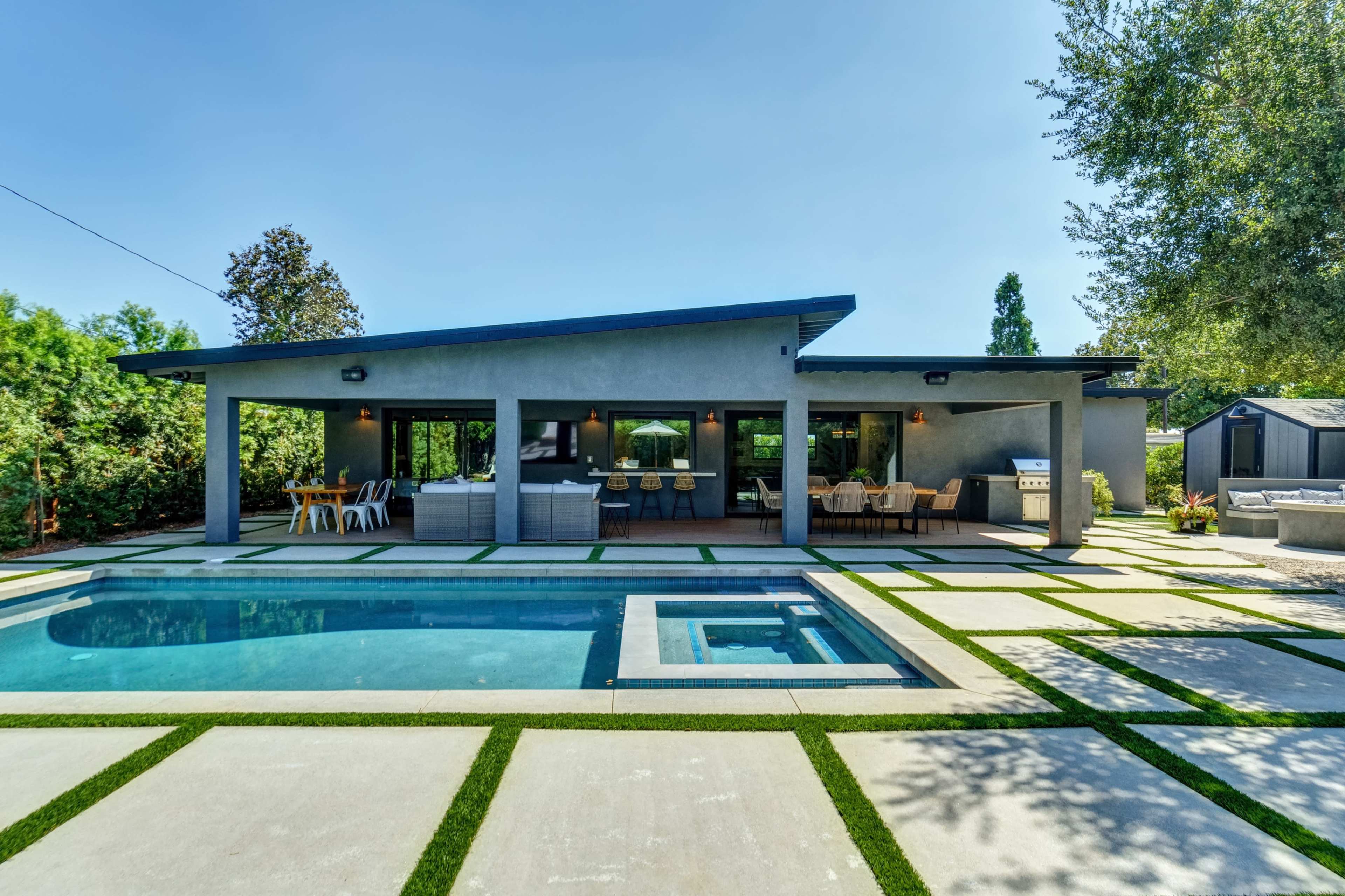A modern backyard with a swimming pool, patio furniture, and a well-maintained lawn surrounded by trees.