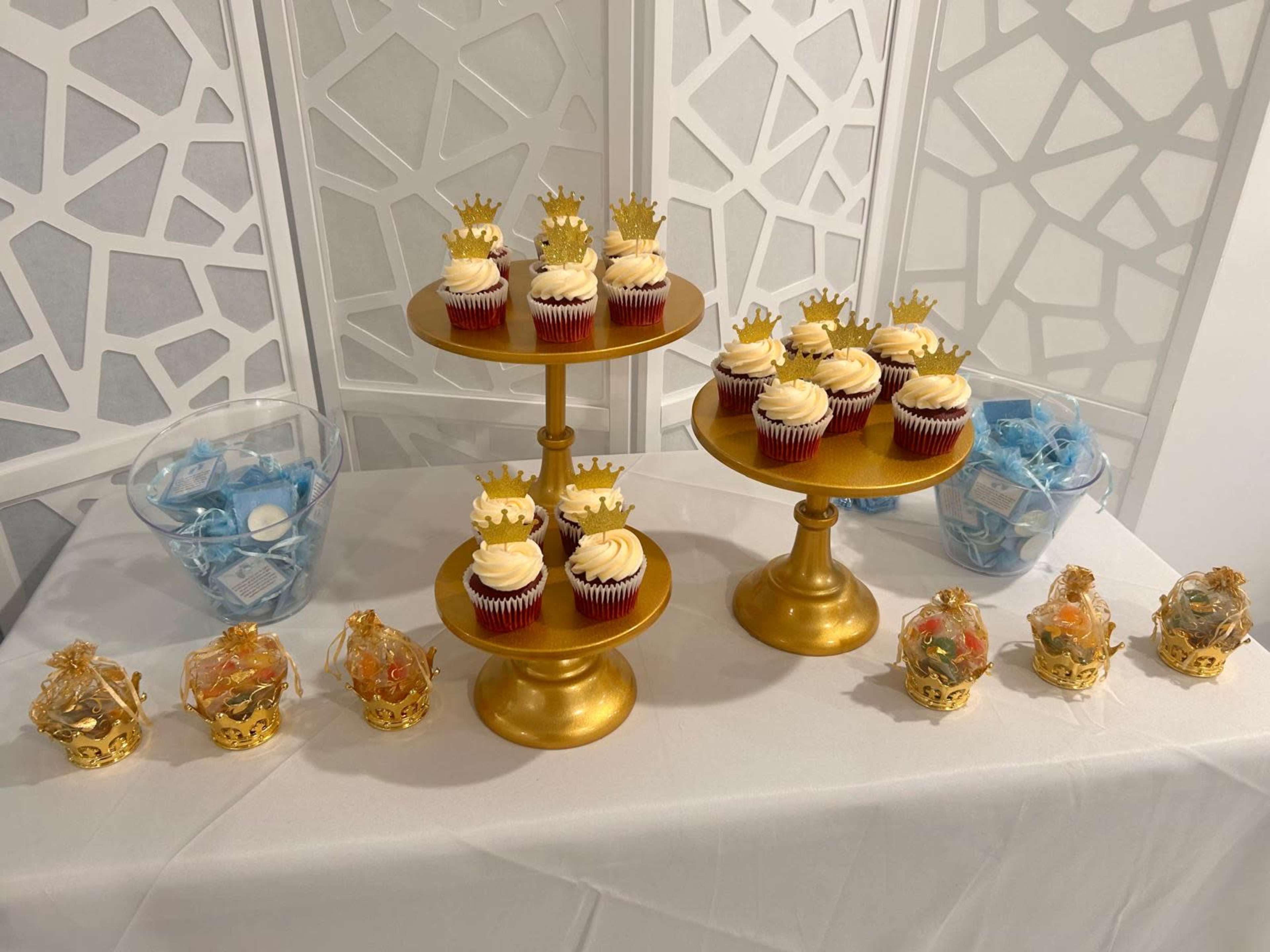 The display features two tiers of red velvet cupcakes with crown-shaped decorations, alongside decorative containers filled with blue and orange candies.