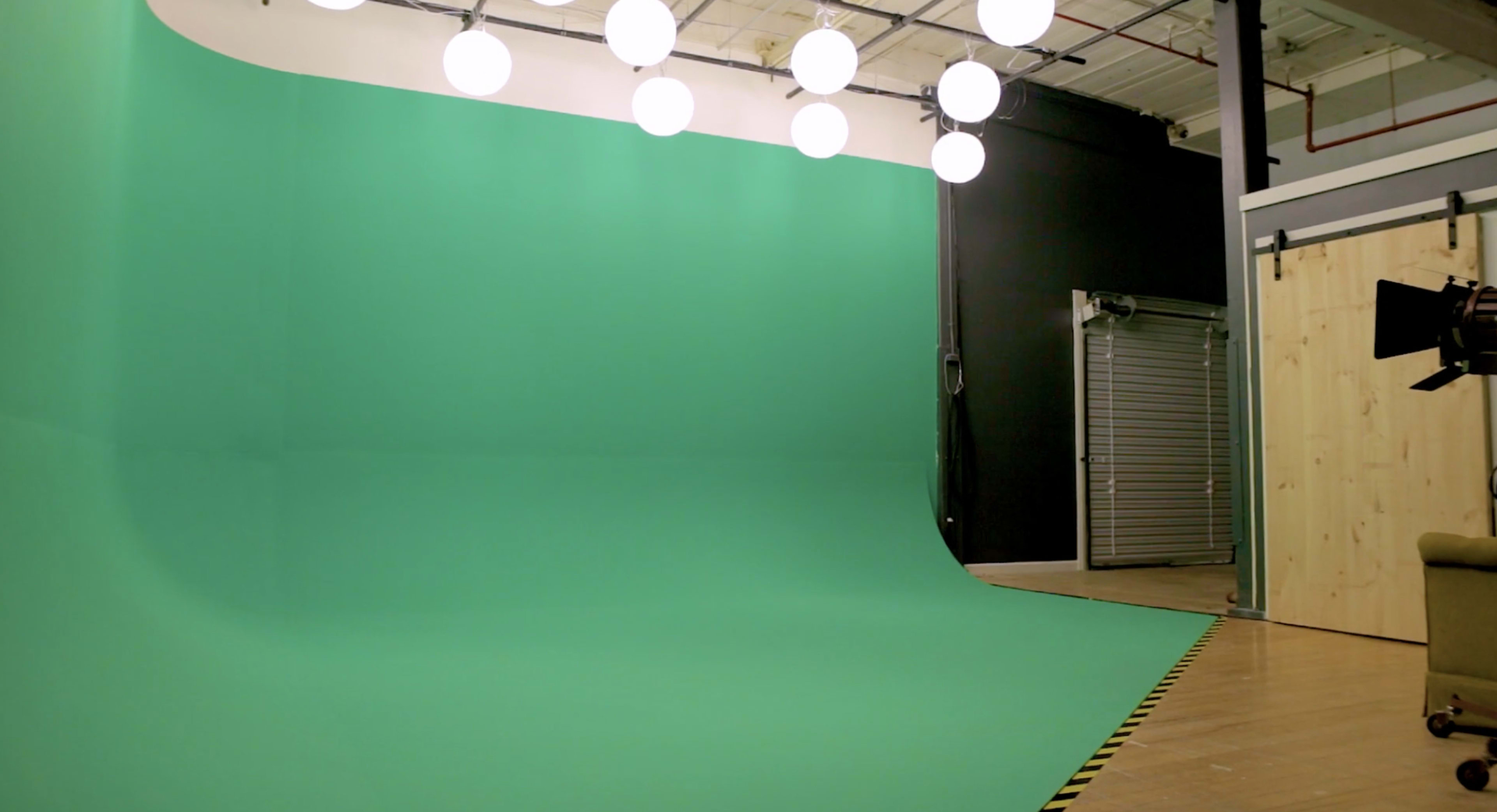 A green screen studio with a curved green backdrop and overhead lights illuminating the space.