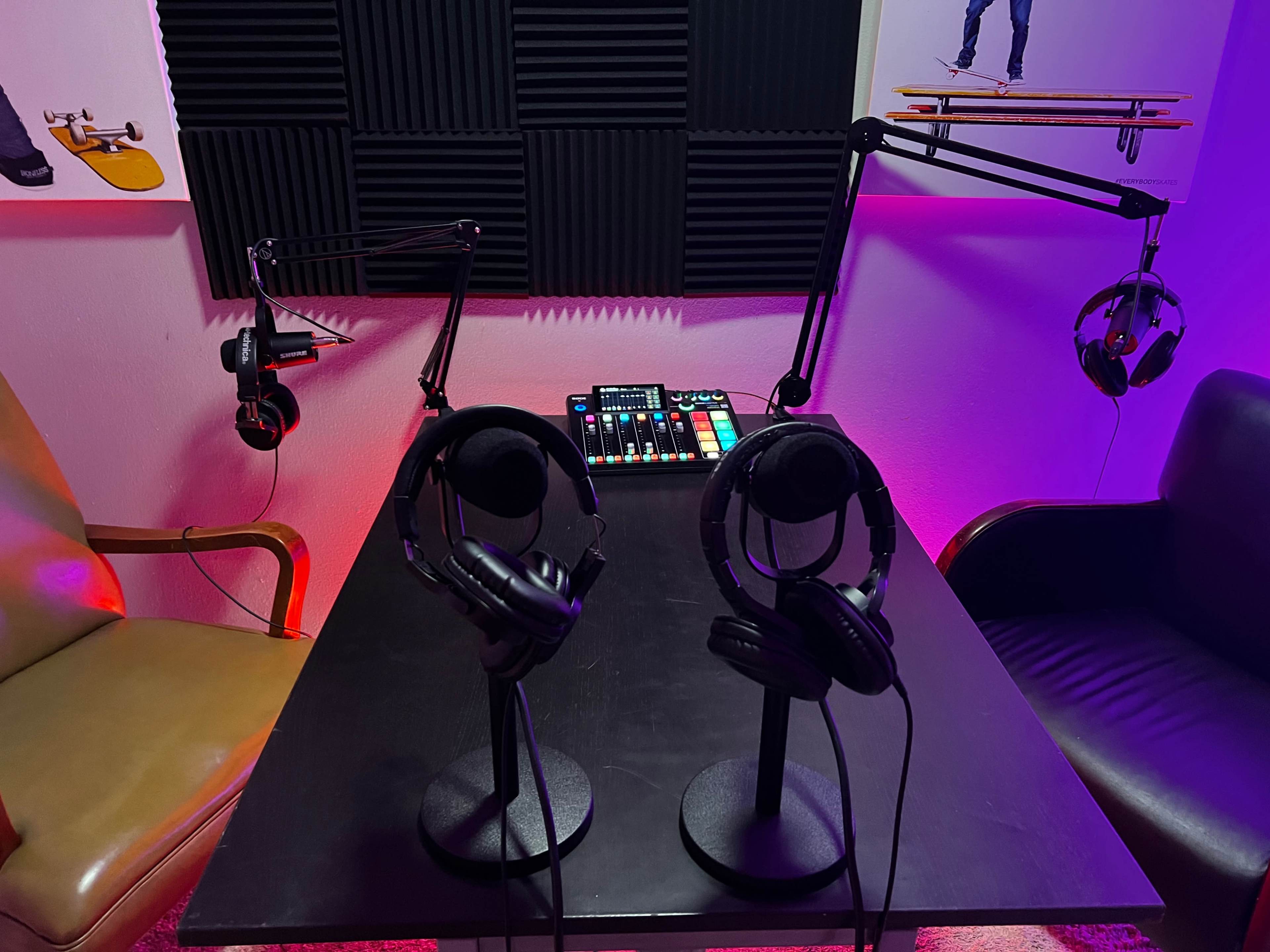 A recording studio setup with two microphones on adjustable arms, two sets of headphones, a sound mixer, and soundproofing panels on the wall.