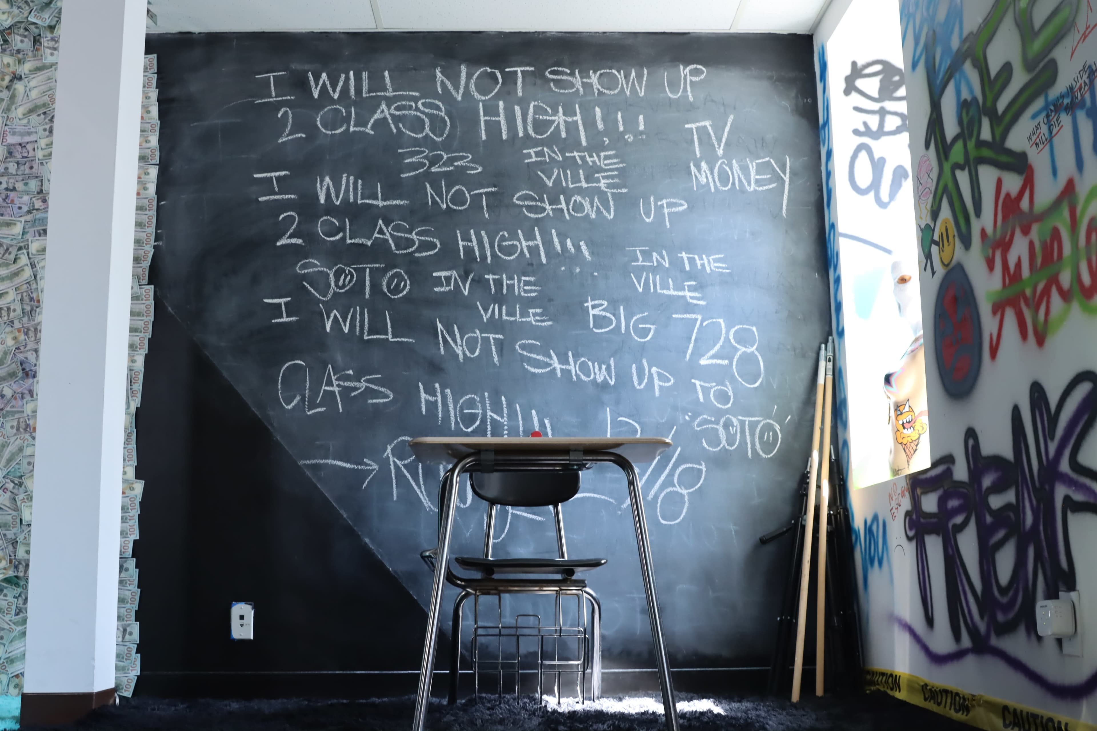 A classroom with a chalkboard wall covered in graffiti-style writing and a single empty desk facing it.