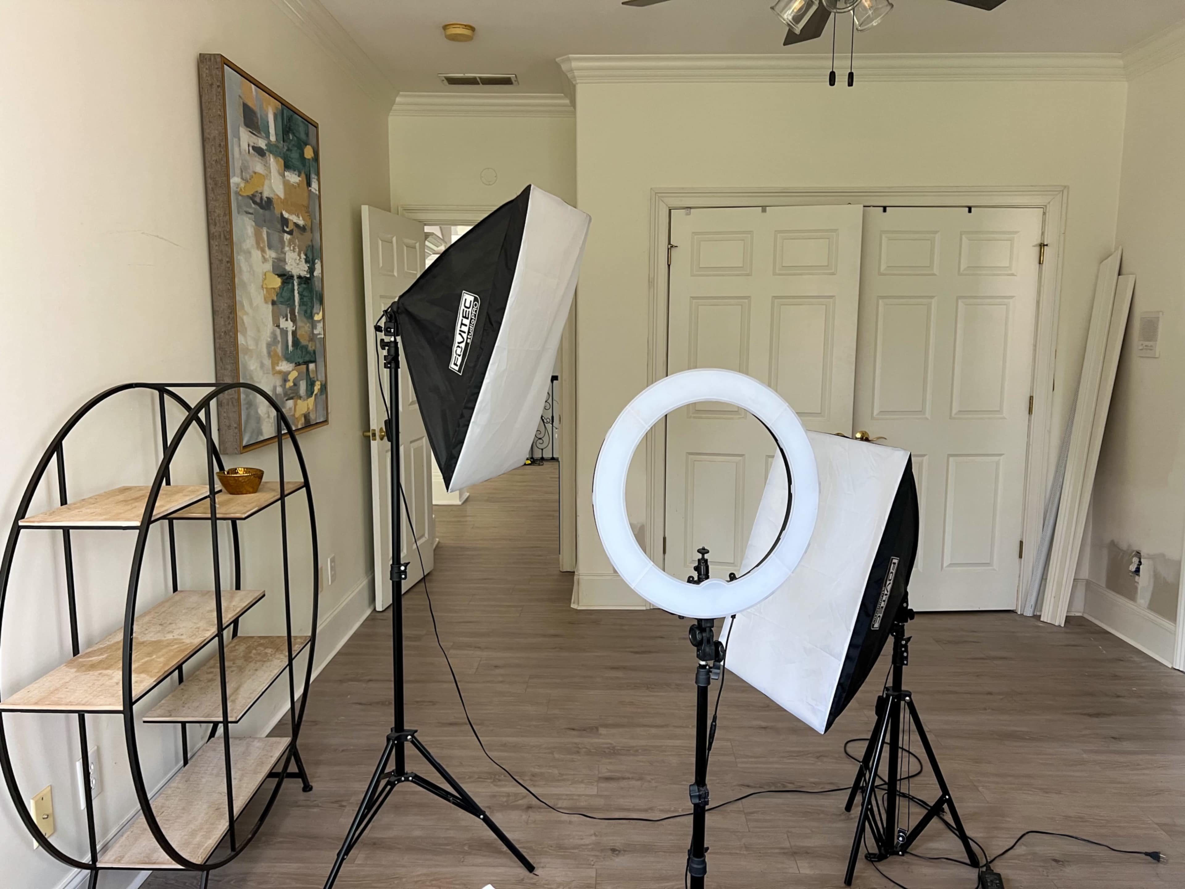 A bright room with a circular light and two softbox lights positioned in front of a shelf and closed double doors.