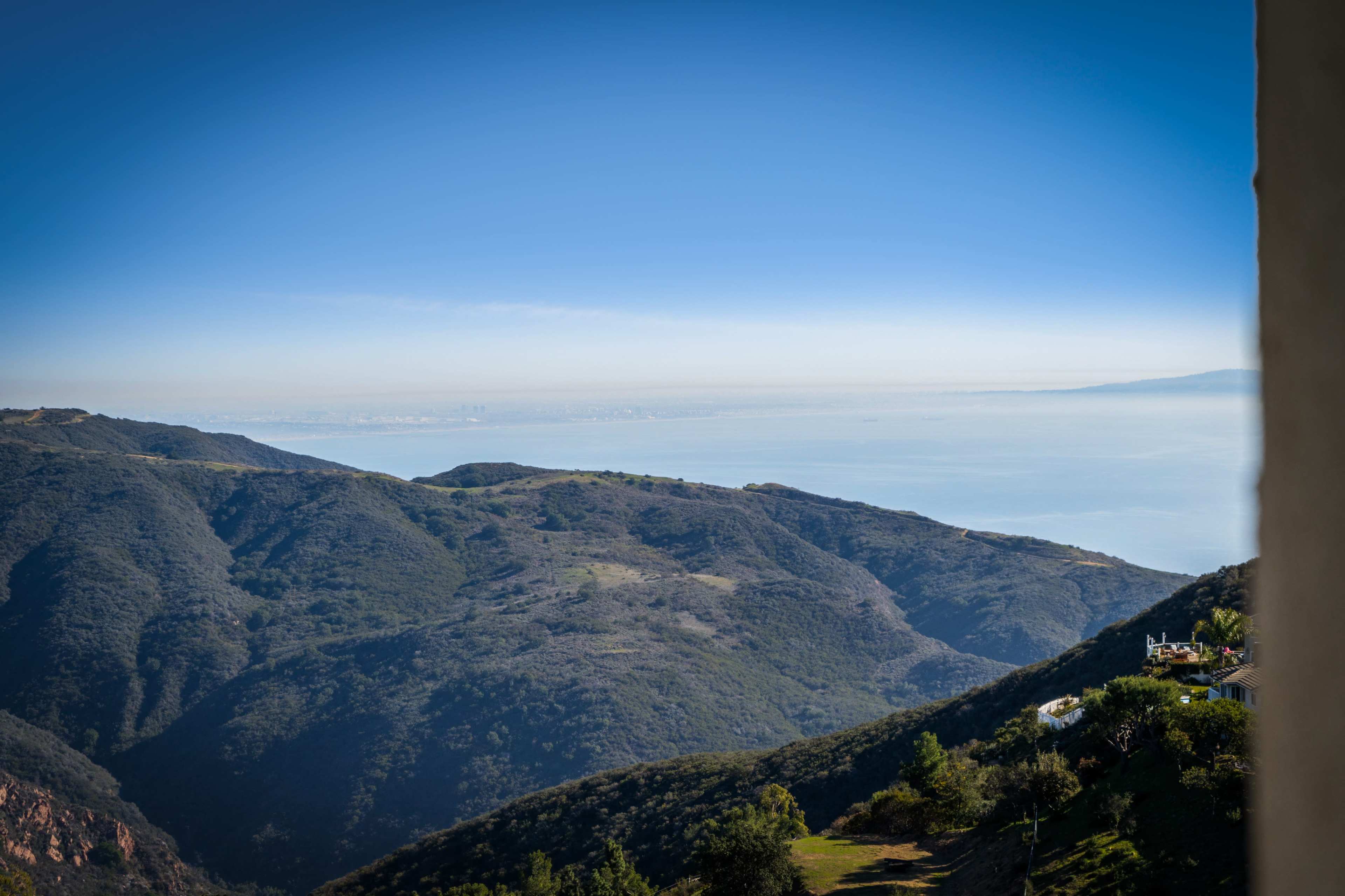 The image shows a coastal view of mountains overlooking a blue ocean and a distant skyline on the horizon.