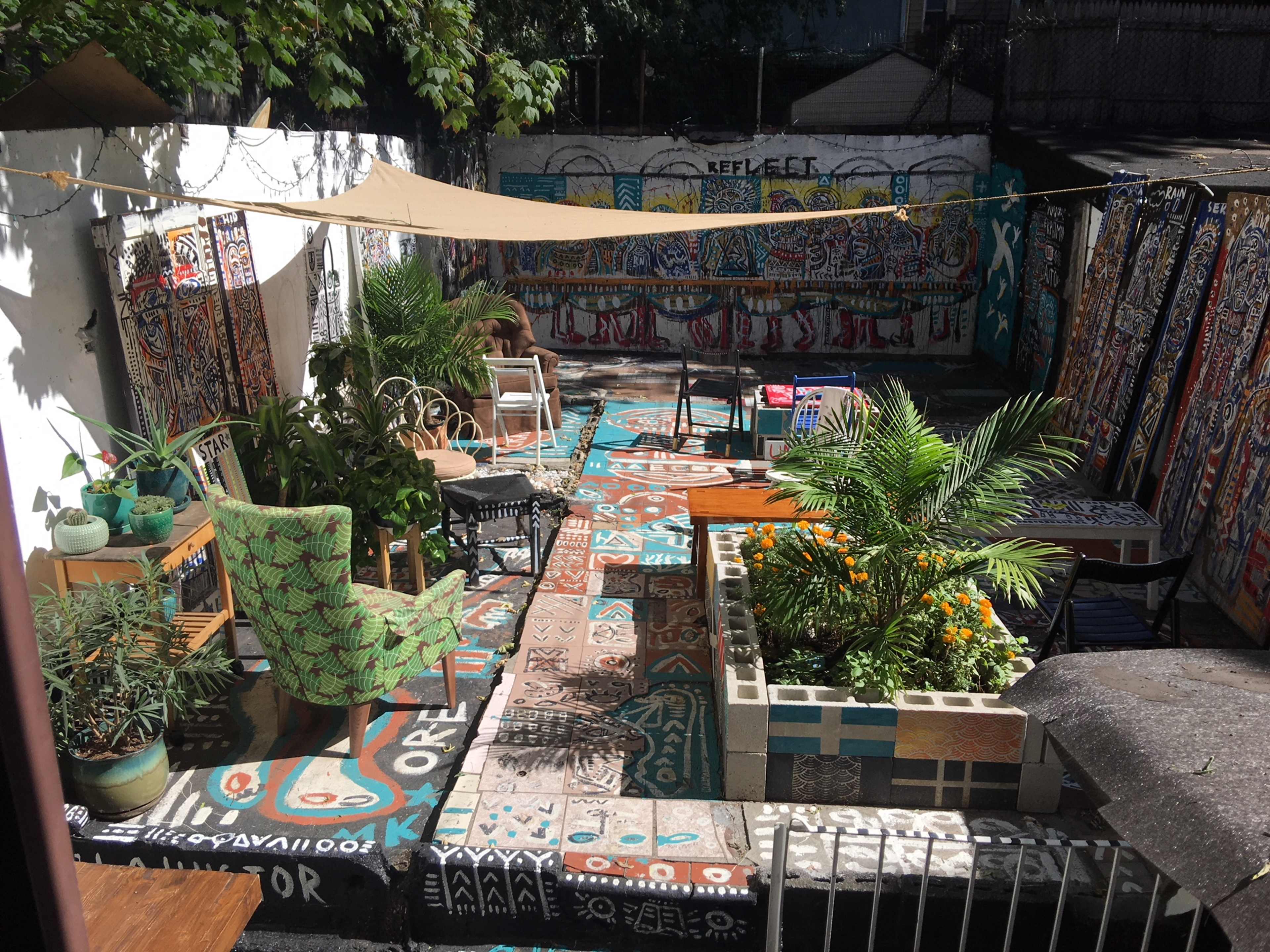 A vibrant outdoor seating area features colorful murals, potted plants, and eclectic furniture arranged on a patterned patio.