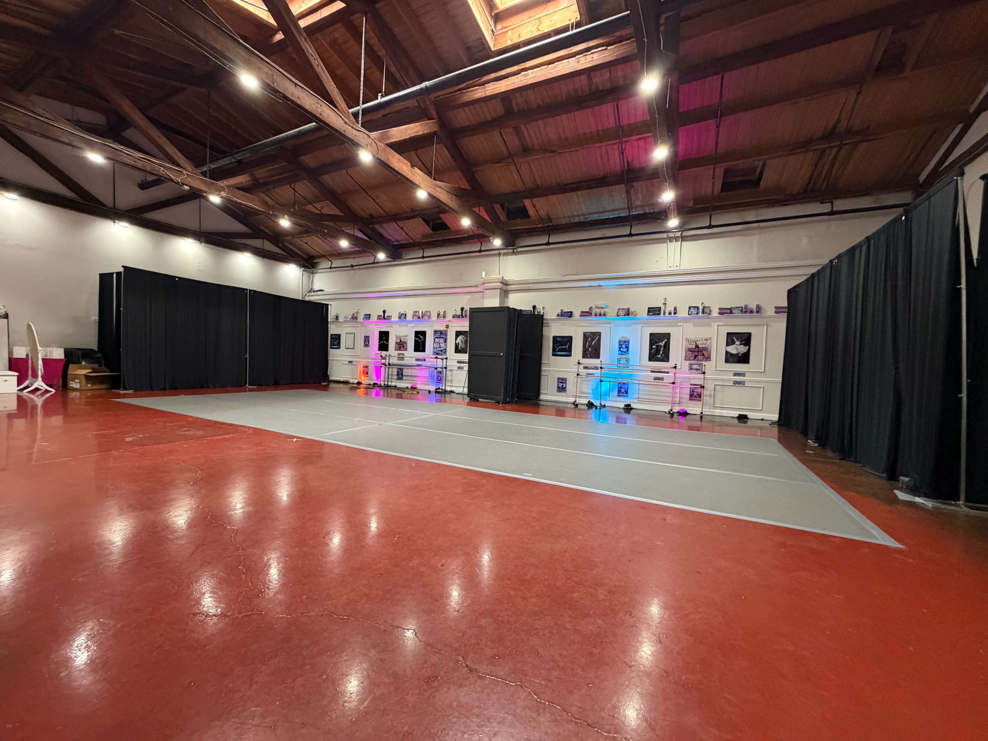 The image shows a spacious studio with a red floor and a gray dance area, surrounded by black curtains and illuminated by colored lights along the walls.