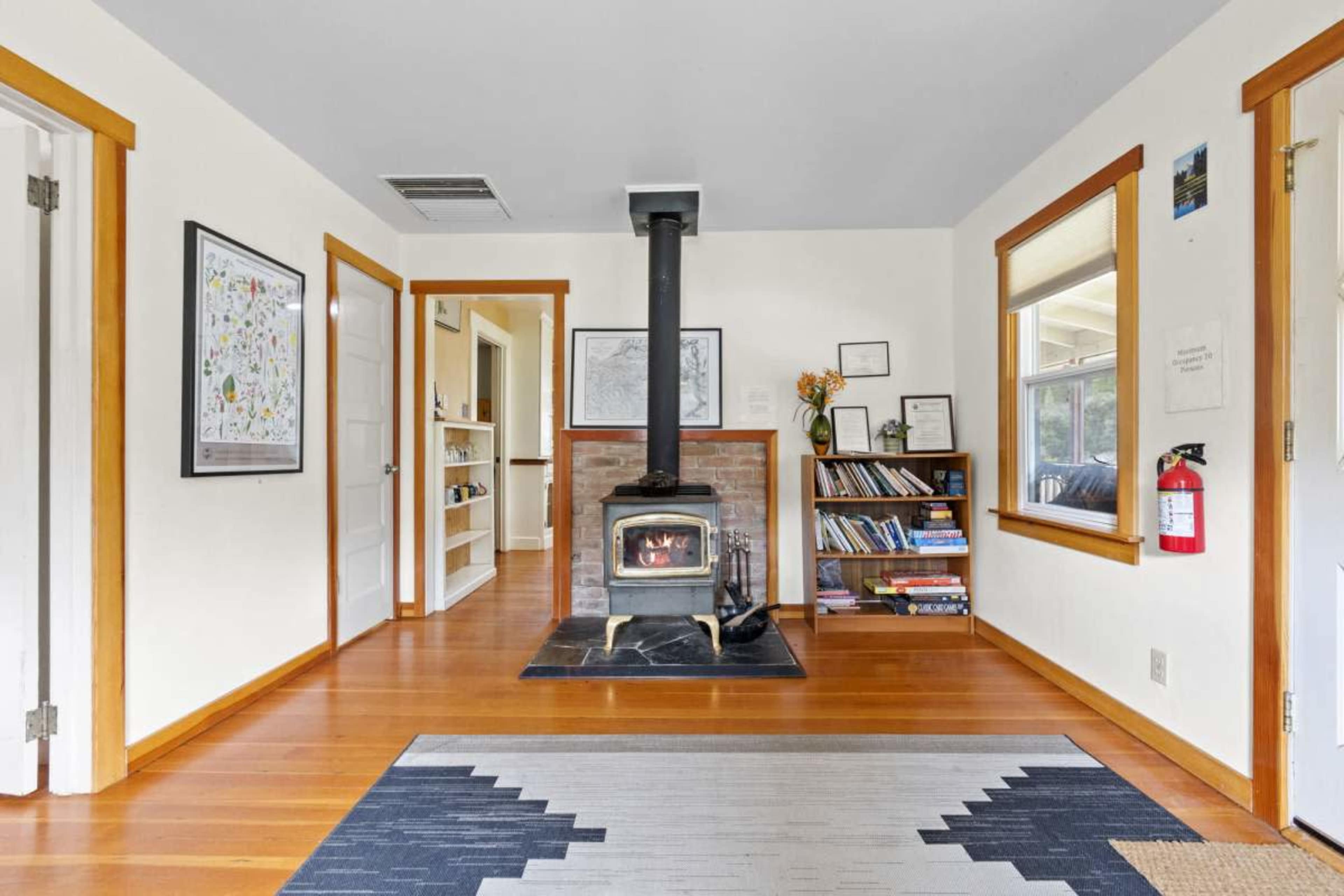 A cozy living room featuring a wood stove on a brick base, surrounded by shelves, framed artwork, and wooden accents.