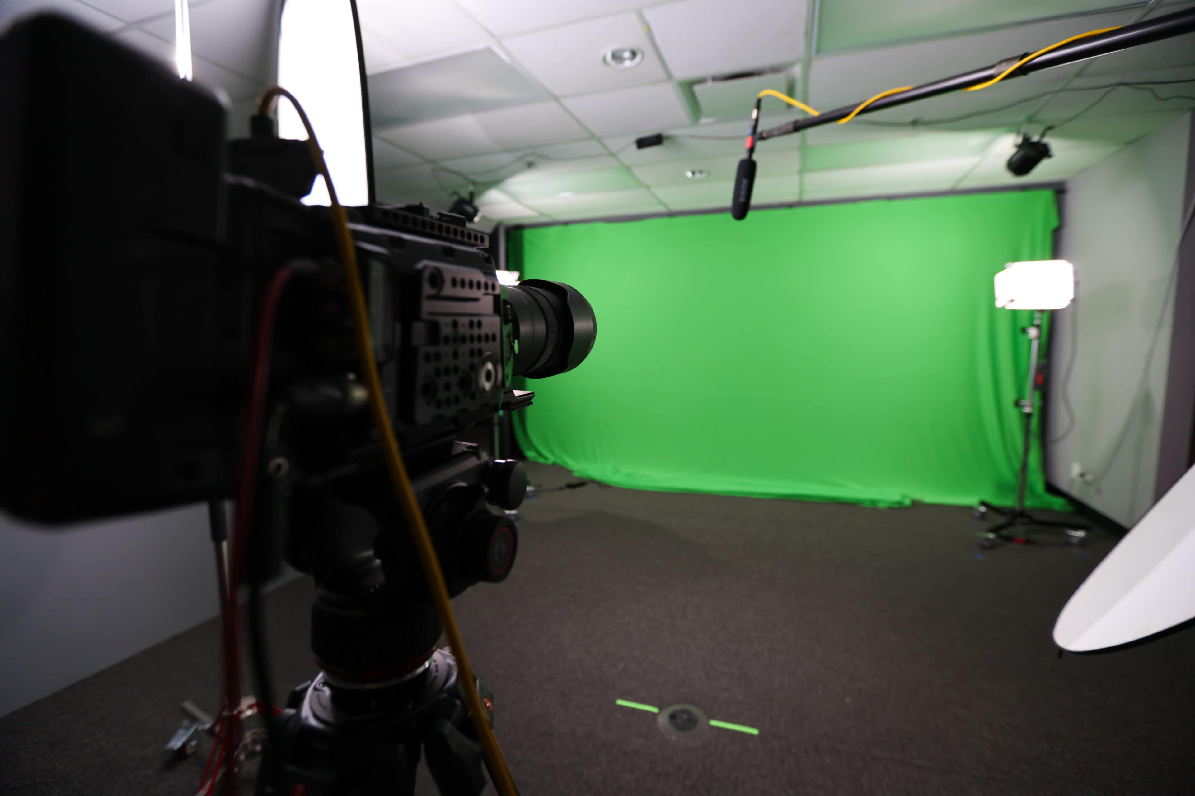 A professional camera is positioned in front of a green screen in a studio setting.