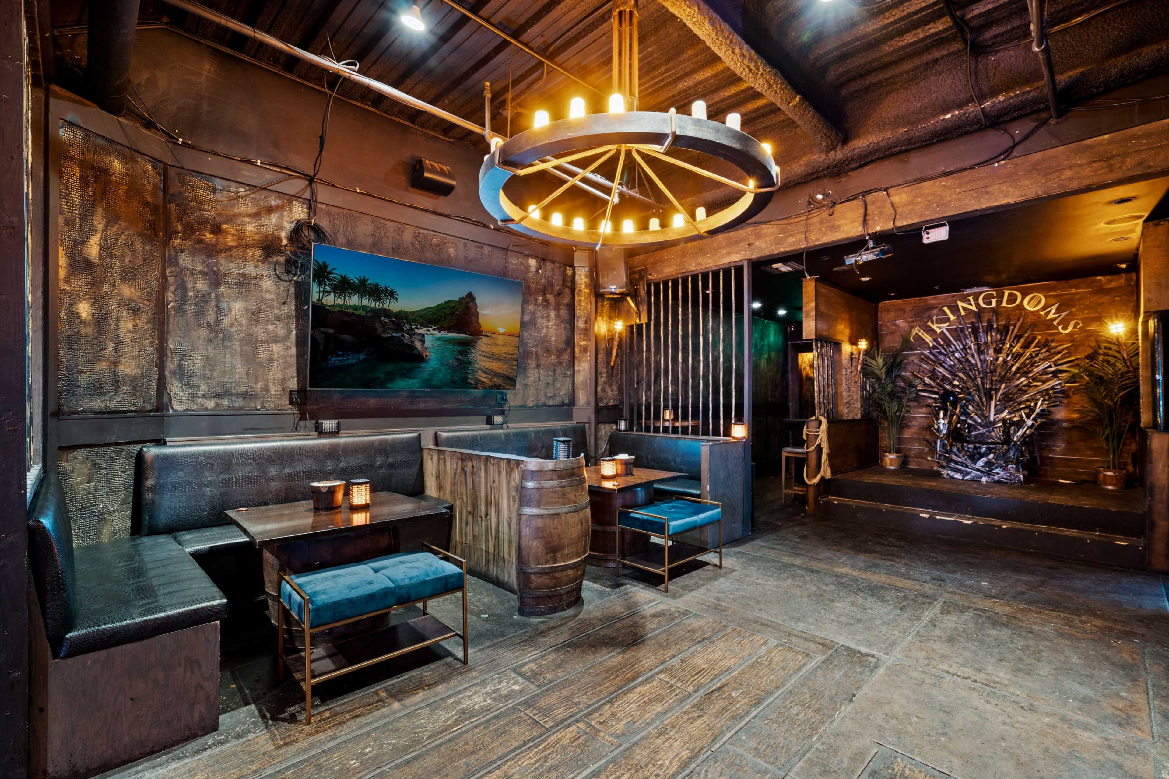 A dimly lit restaurant interior featuring wooden tables and benches, a large chandelier, and tropical-themed decor on the walls.