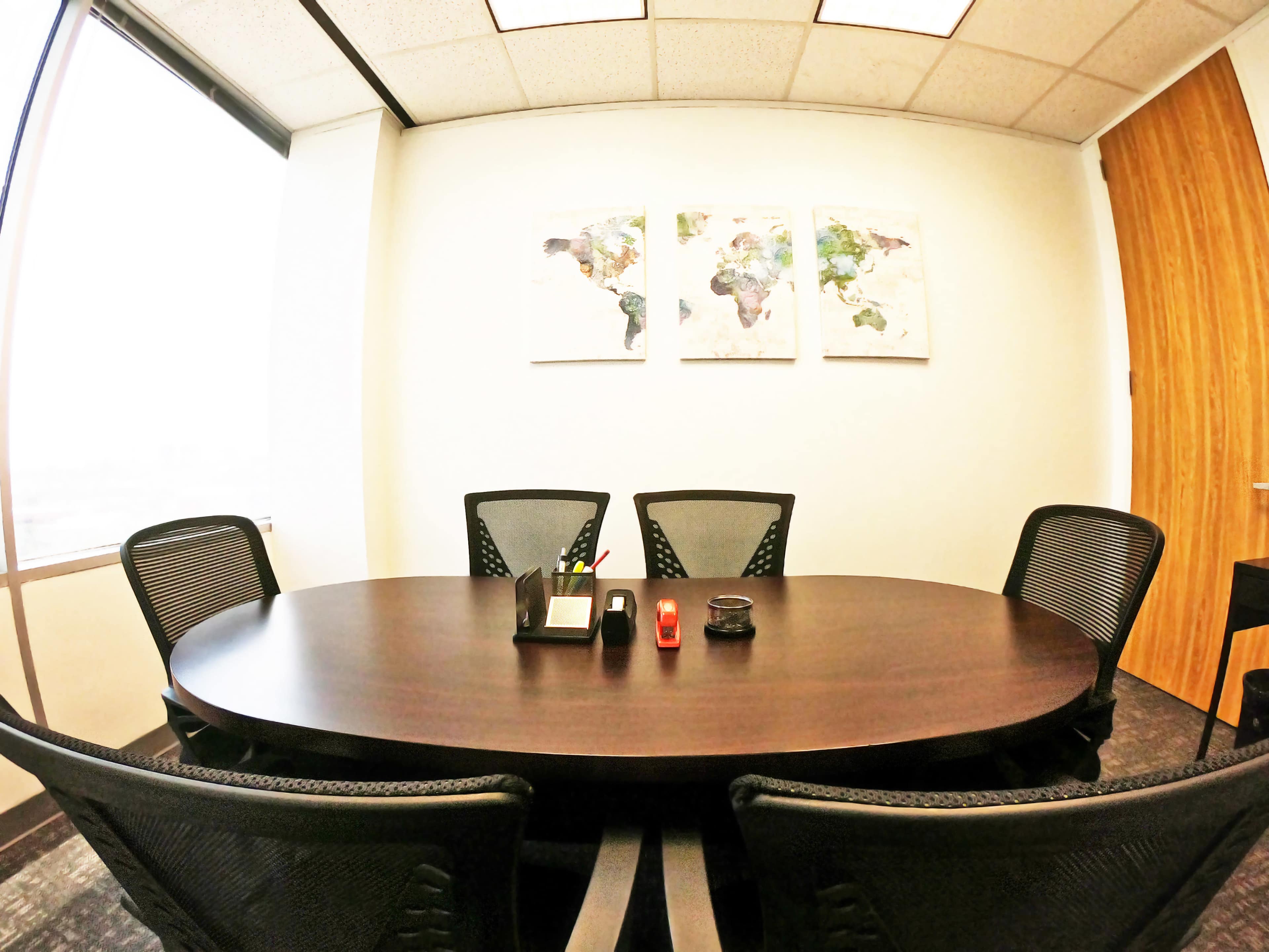 A round conference table surrounded by four black mesh chairs is situated in a well-lit office with a map artwork on the wall.
