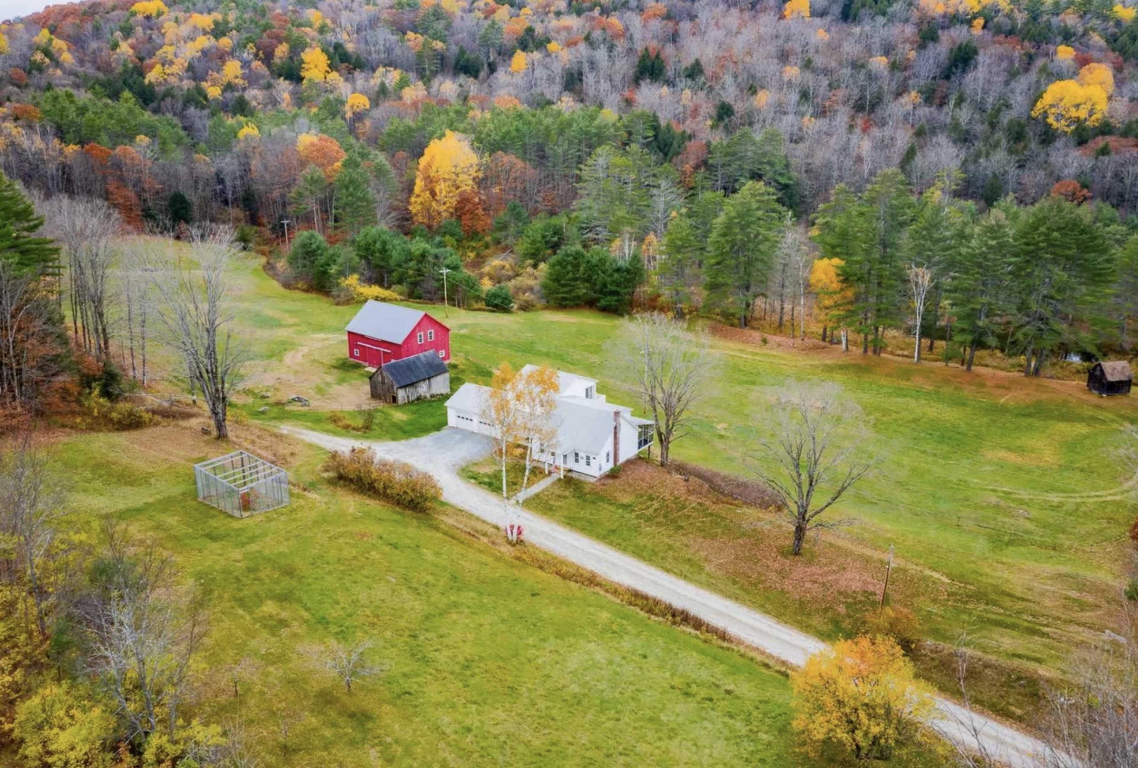 A rural landscape with a white house, a red barn, and a dirt road surrounded by colorful autumn trees.