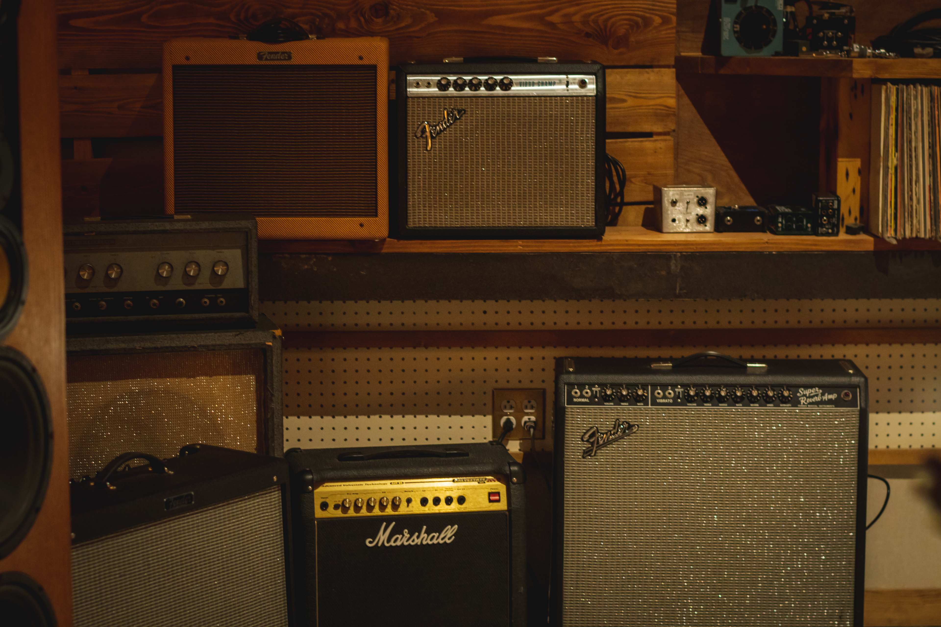 A collection of various guitar amplifiers arranged on shelving in a studio or practice space.