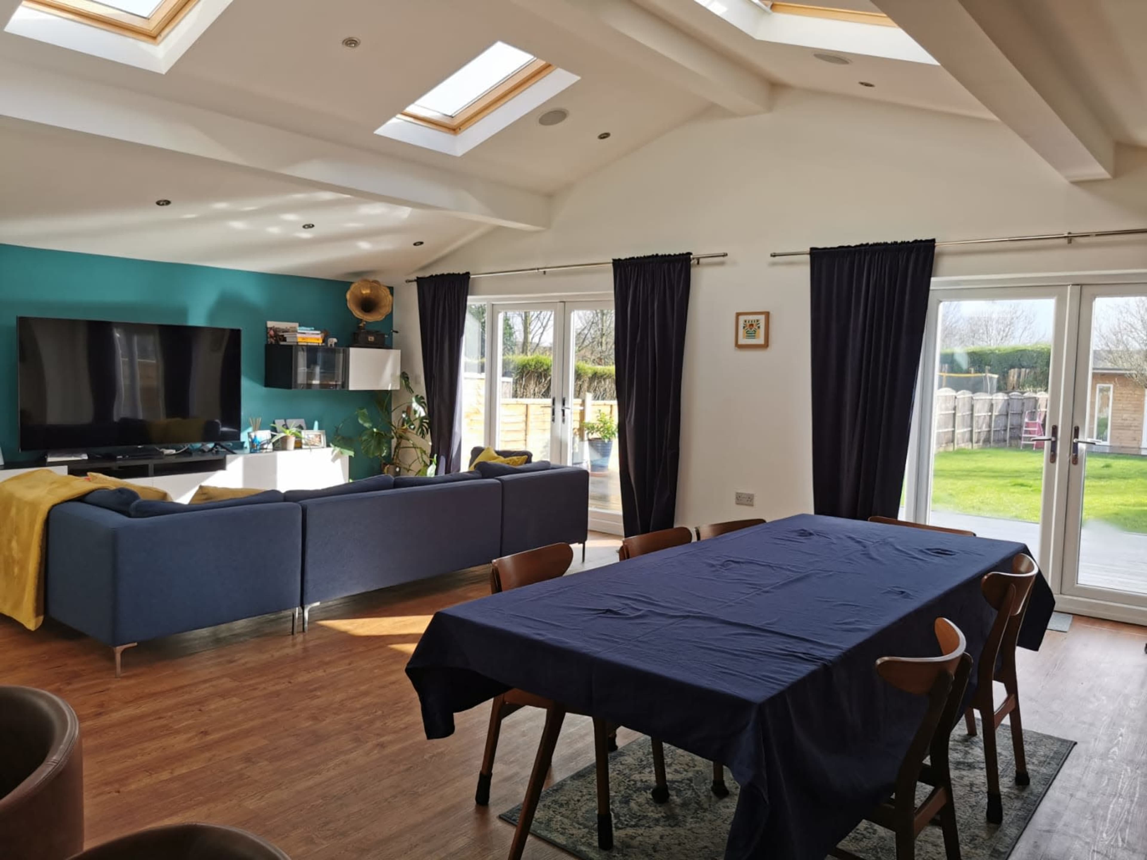 A spacious living area with a large dining table, a blue couch, a flat-screen TV, and sliding glass doors leading to a backyard.