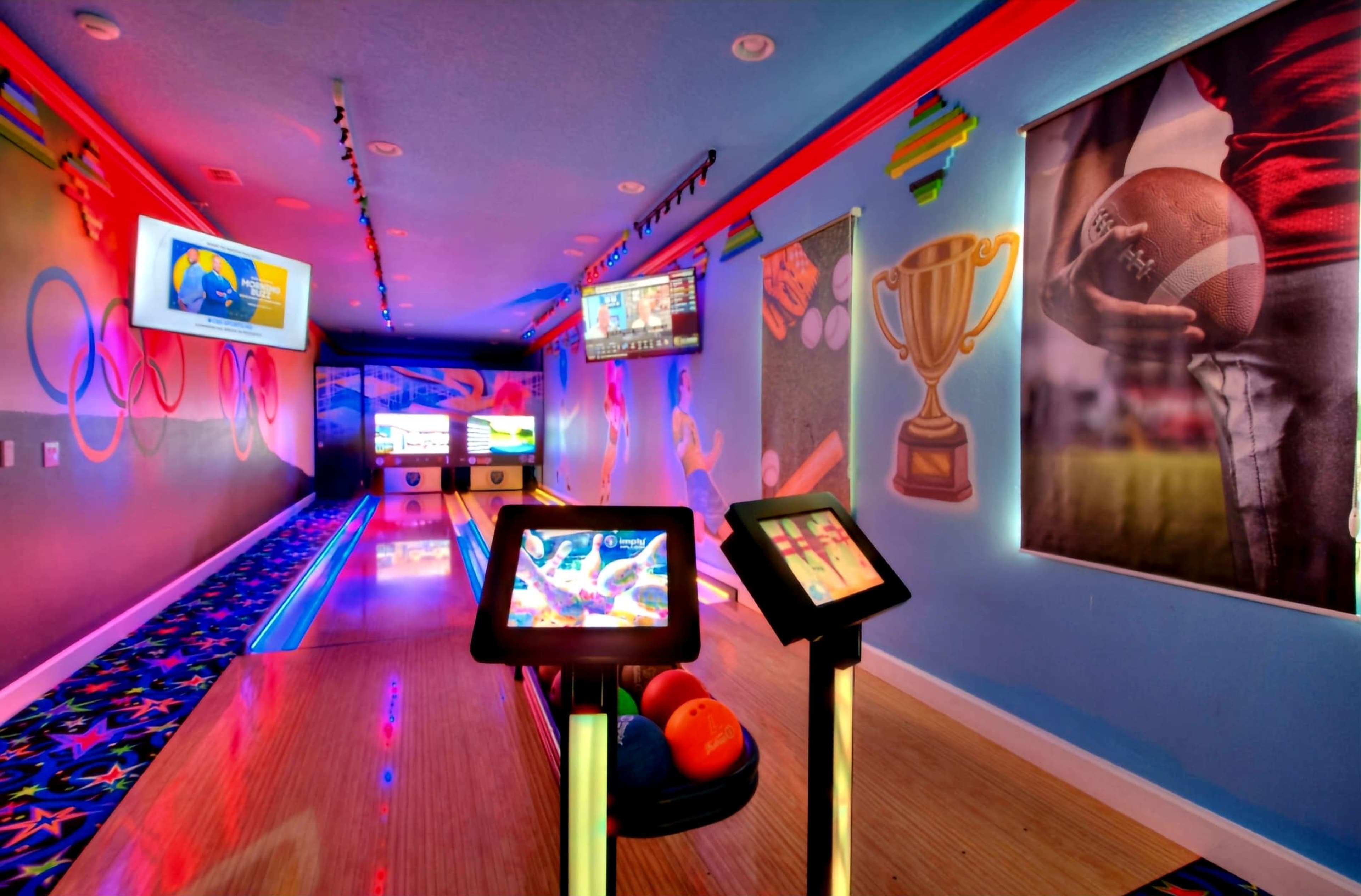 A brightly colored bowling alley with video screens, vibrant wall murals, and bowling balls lined up near the lanes.