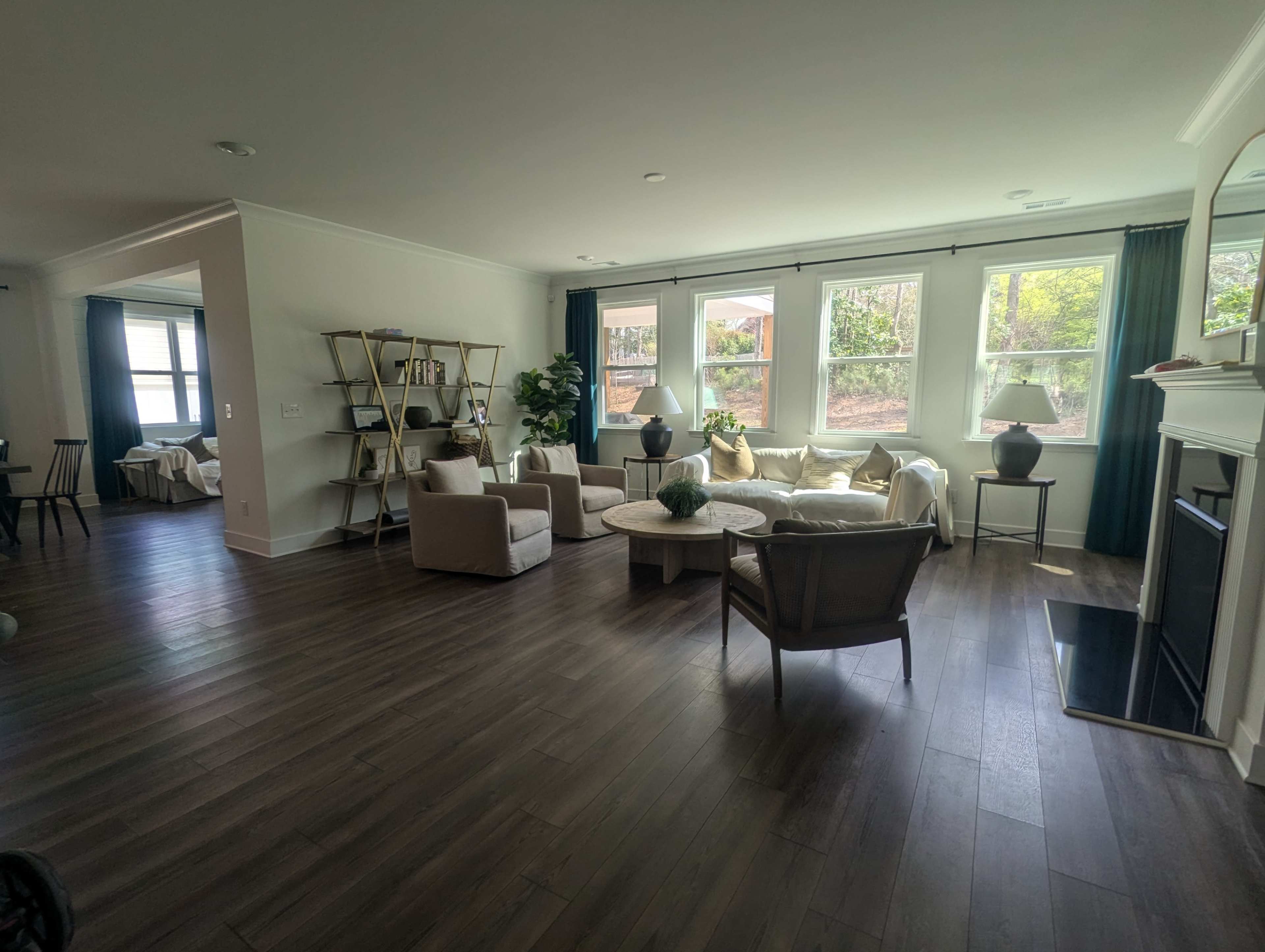 The image shows a modern living room with light-colored furniture, large windows, and a fireplace, featuring a cozy seating arrangement and decorative plants.