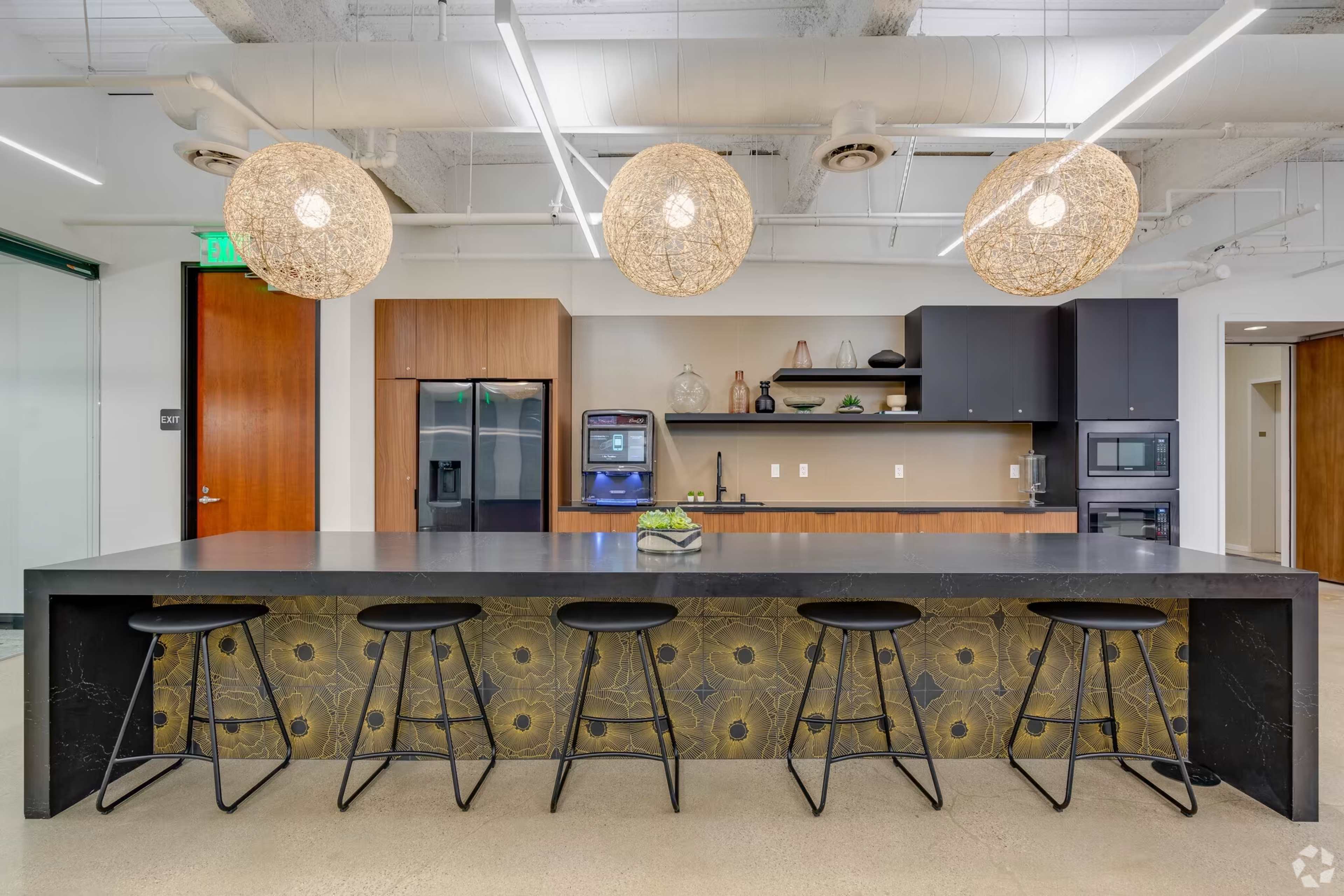 A modern kitchen with a large dark countertop, bar stools, and stylish pendant lights overhead.