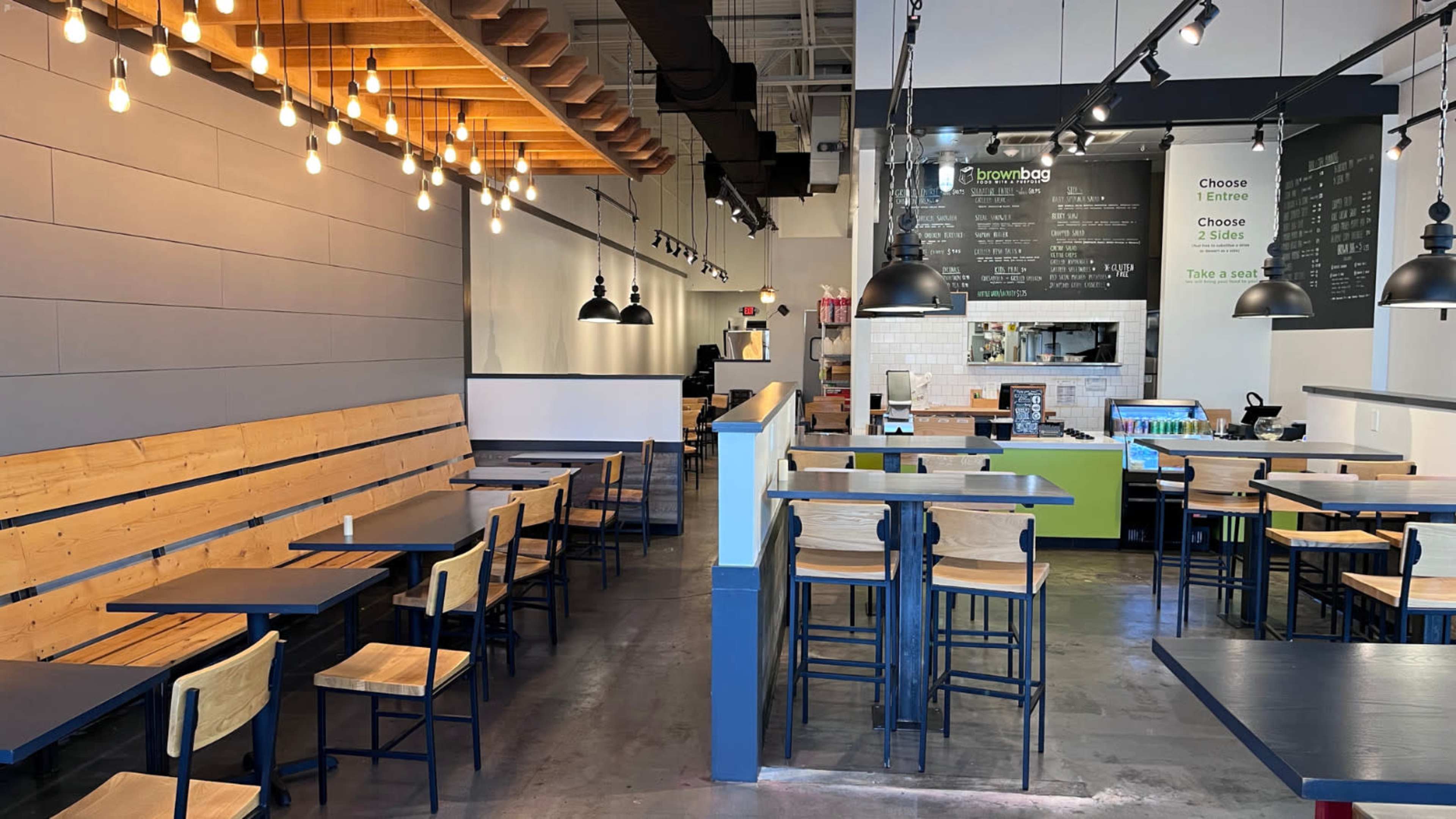 A modern, minimalist restaurant interior with wooden benches, tall tables, and a service counter displaying a menu.