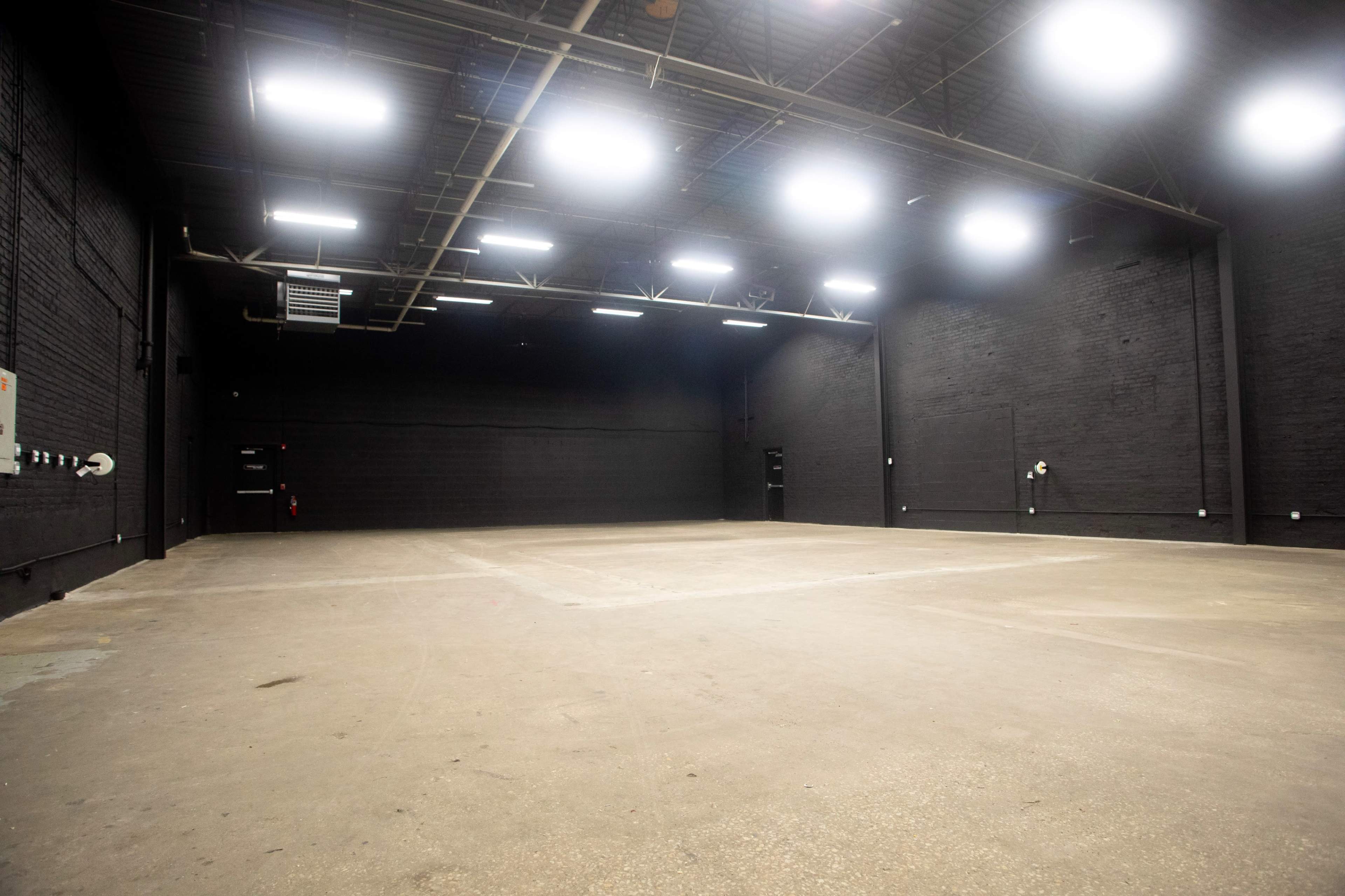 The image shows a large, empty industrial space with black walls and bright overhead lights.