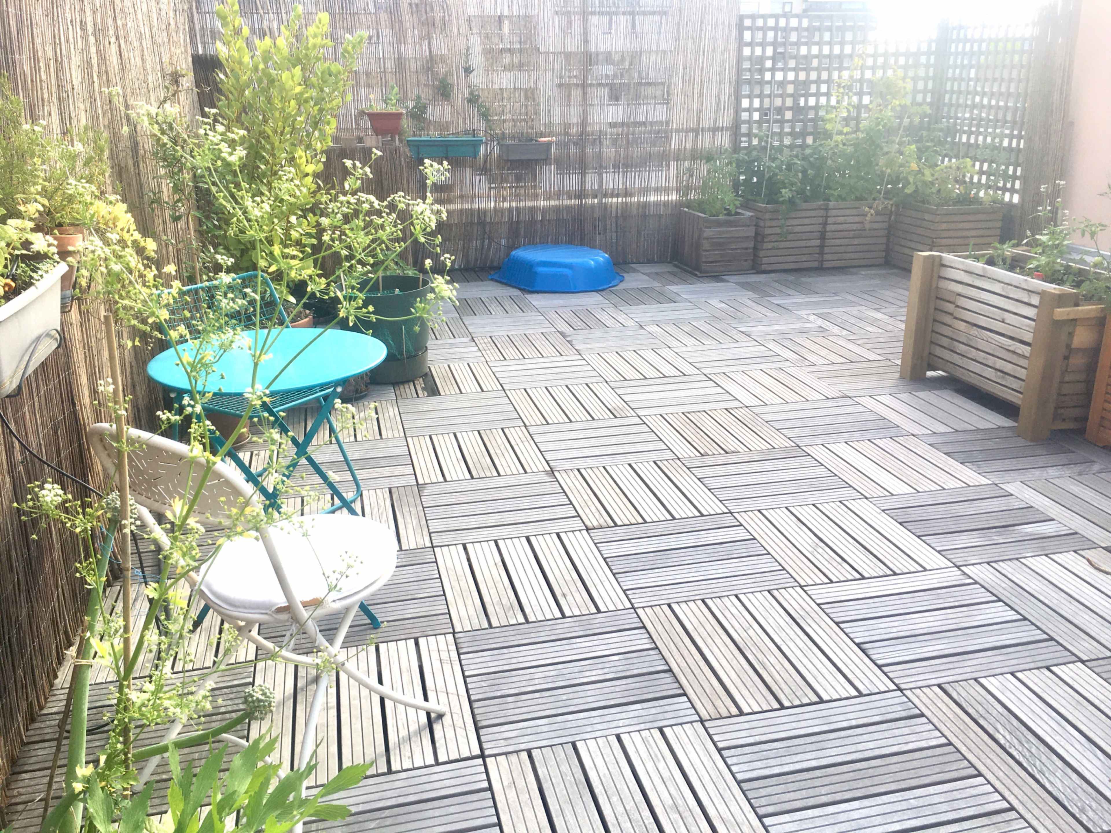 A patio area featuring wooden decking, potted plants, a blue dog water bowl, and two small tables with chairs.
