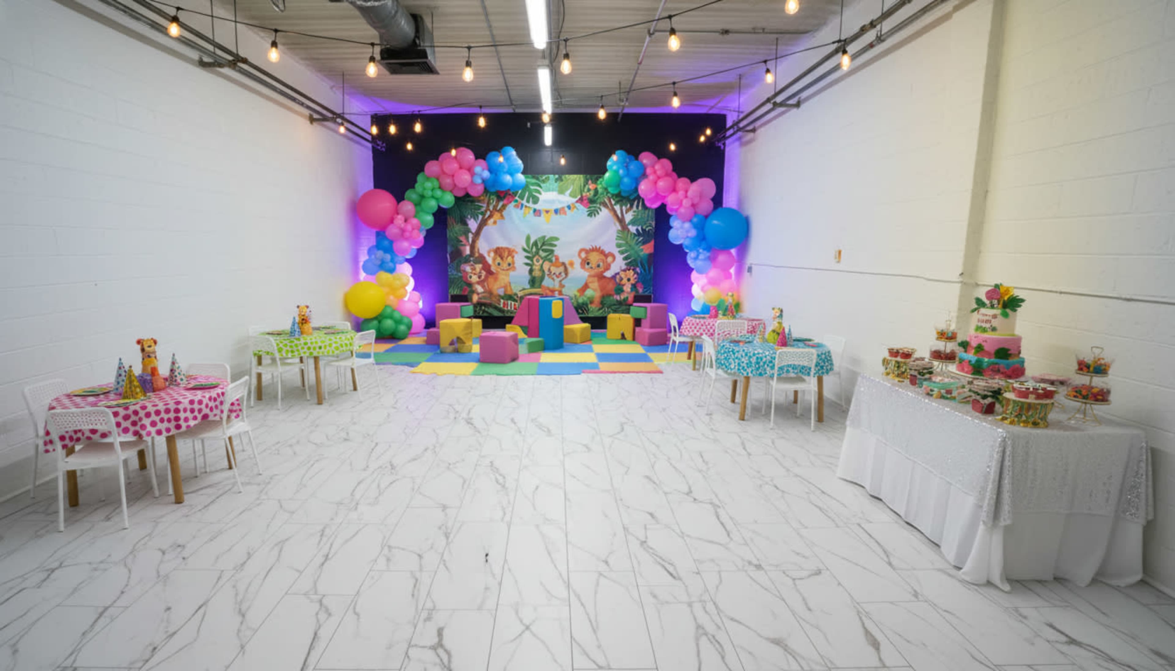 A bright event space is decorated with colorful balloons and themed tables, featuring a playful backdrop and various dessert displays.