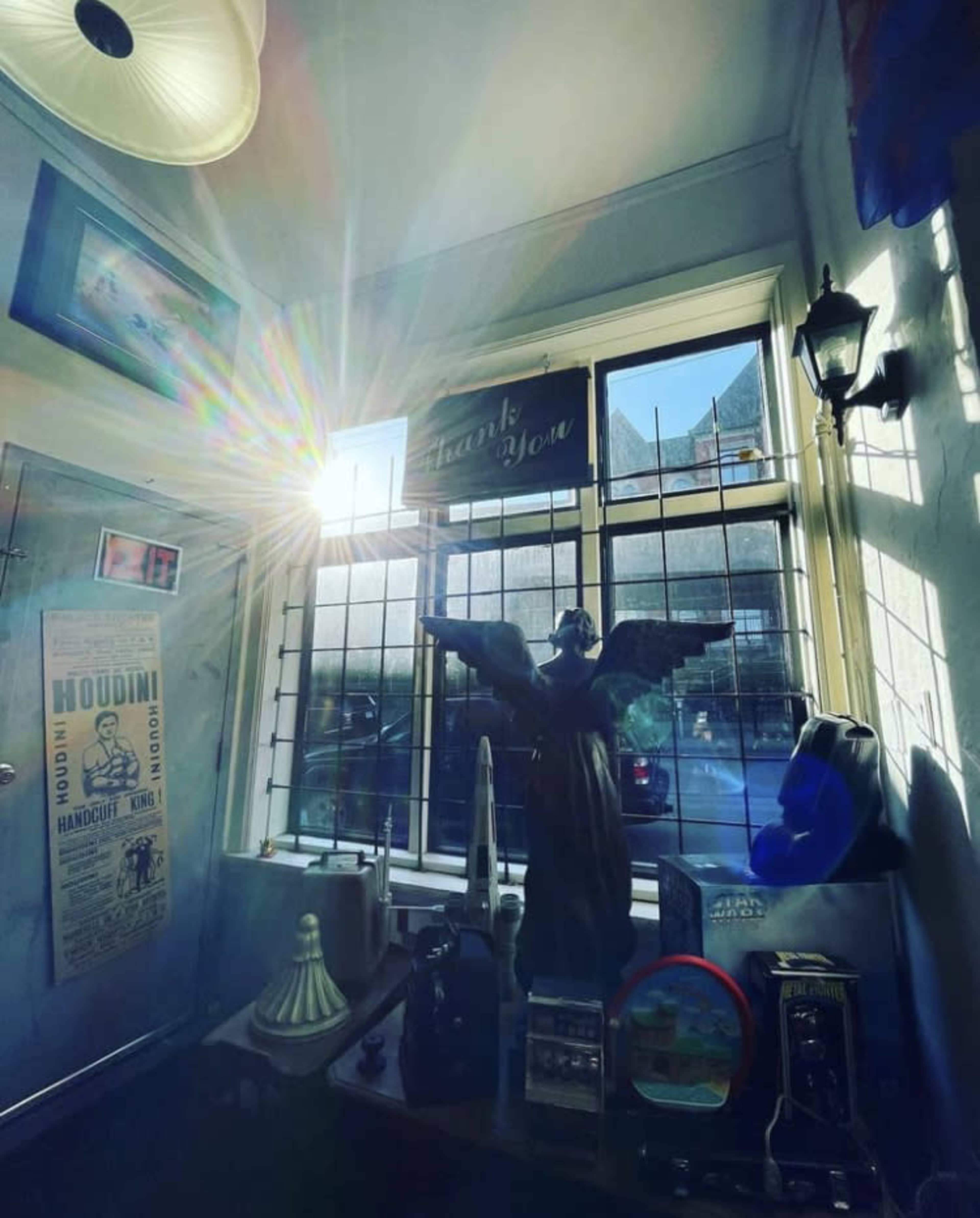 A beam of sunlight shines through a window, illuminating a room with various artifacts, including a statue of an angel and framed pictures on the walls.