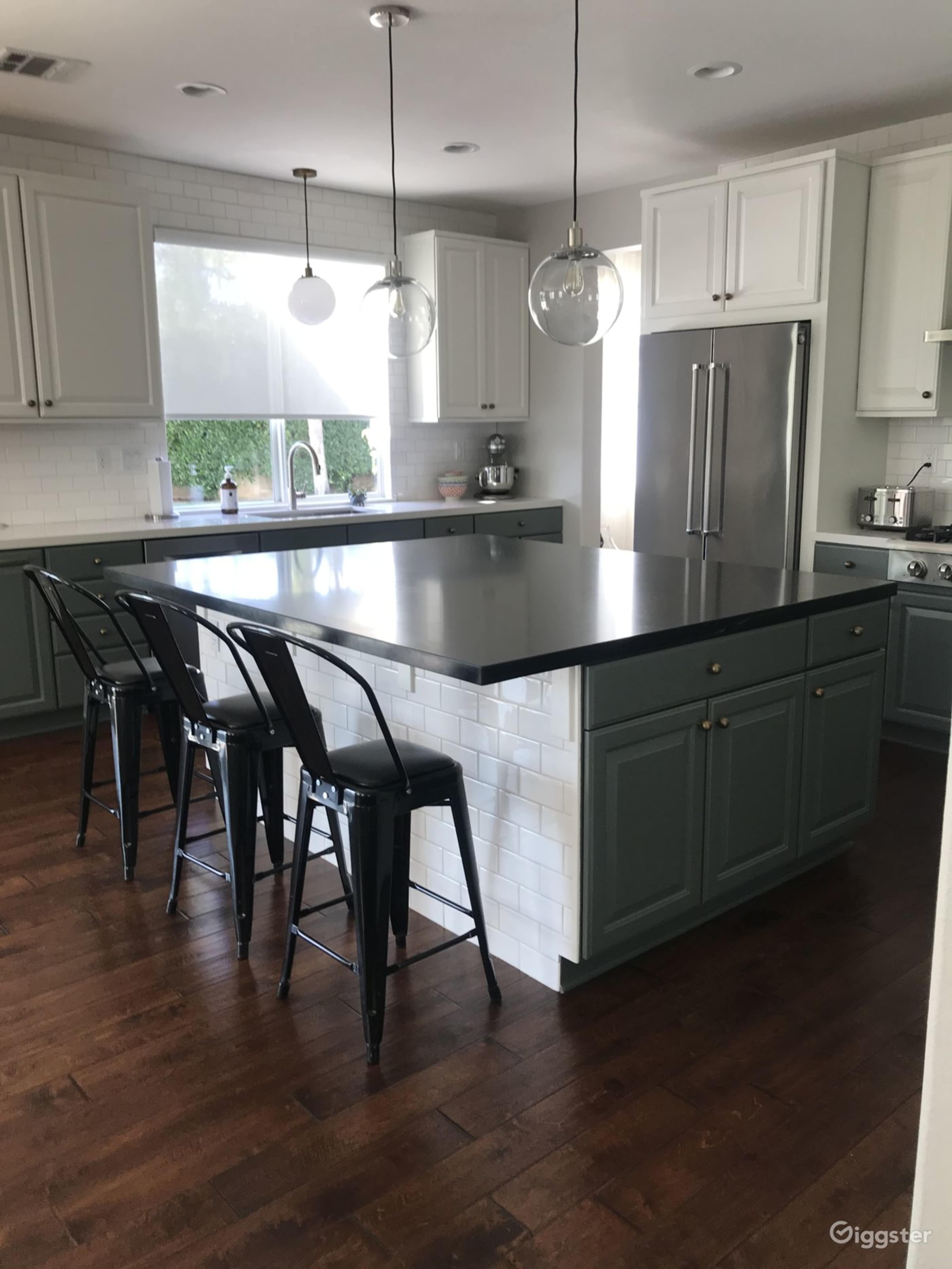 A modern kitchen features a central island with black countertops, gray cabinetry, and four metal bar stools.