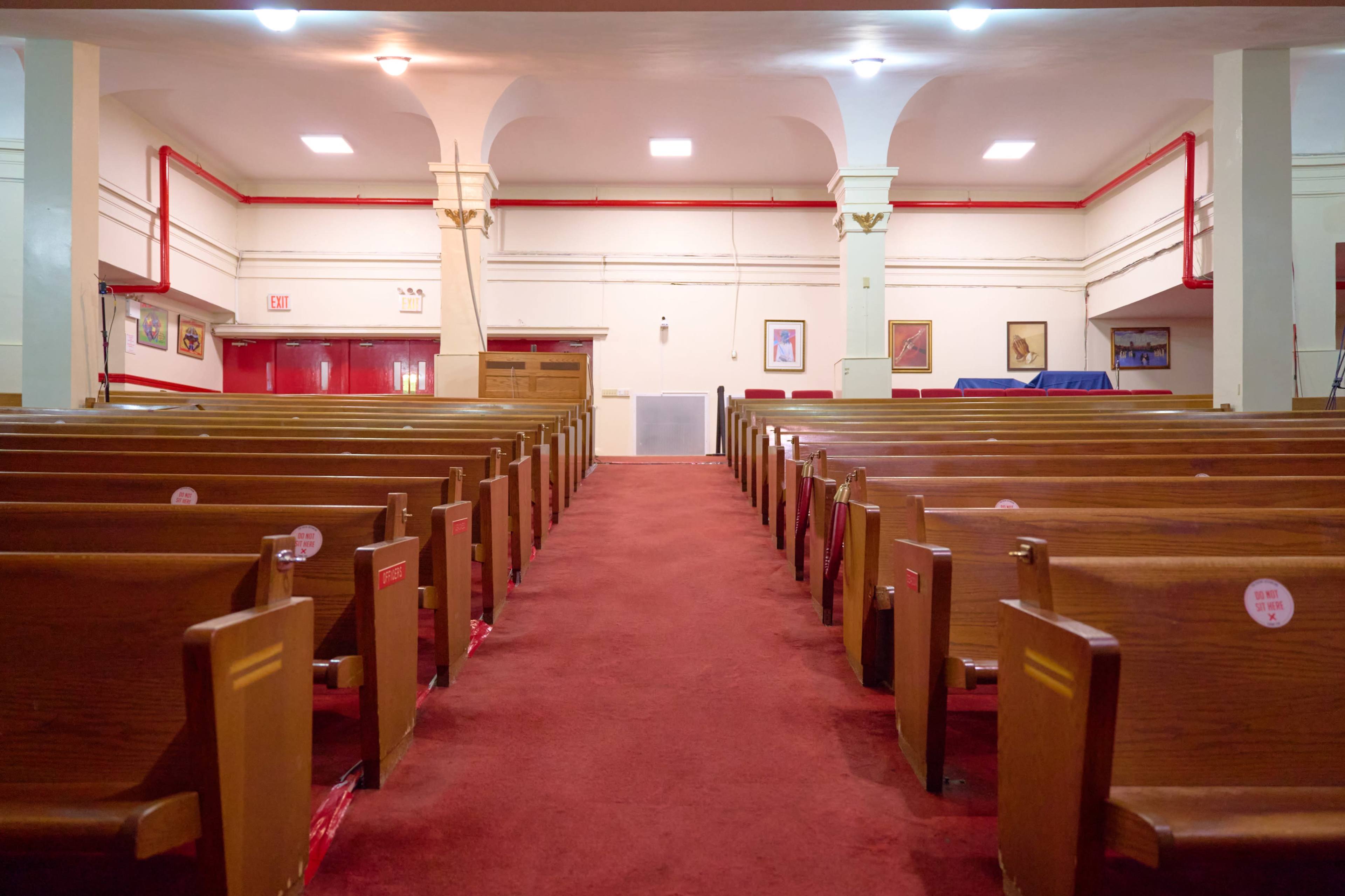 The image shows a spacious interior of a church with rows of wooden pews facing a central aisle and a small altar area at the front.