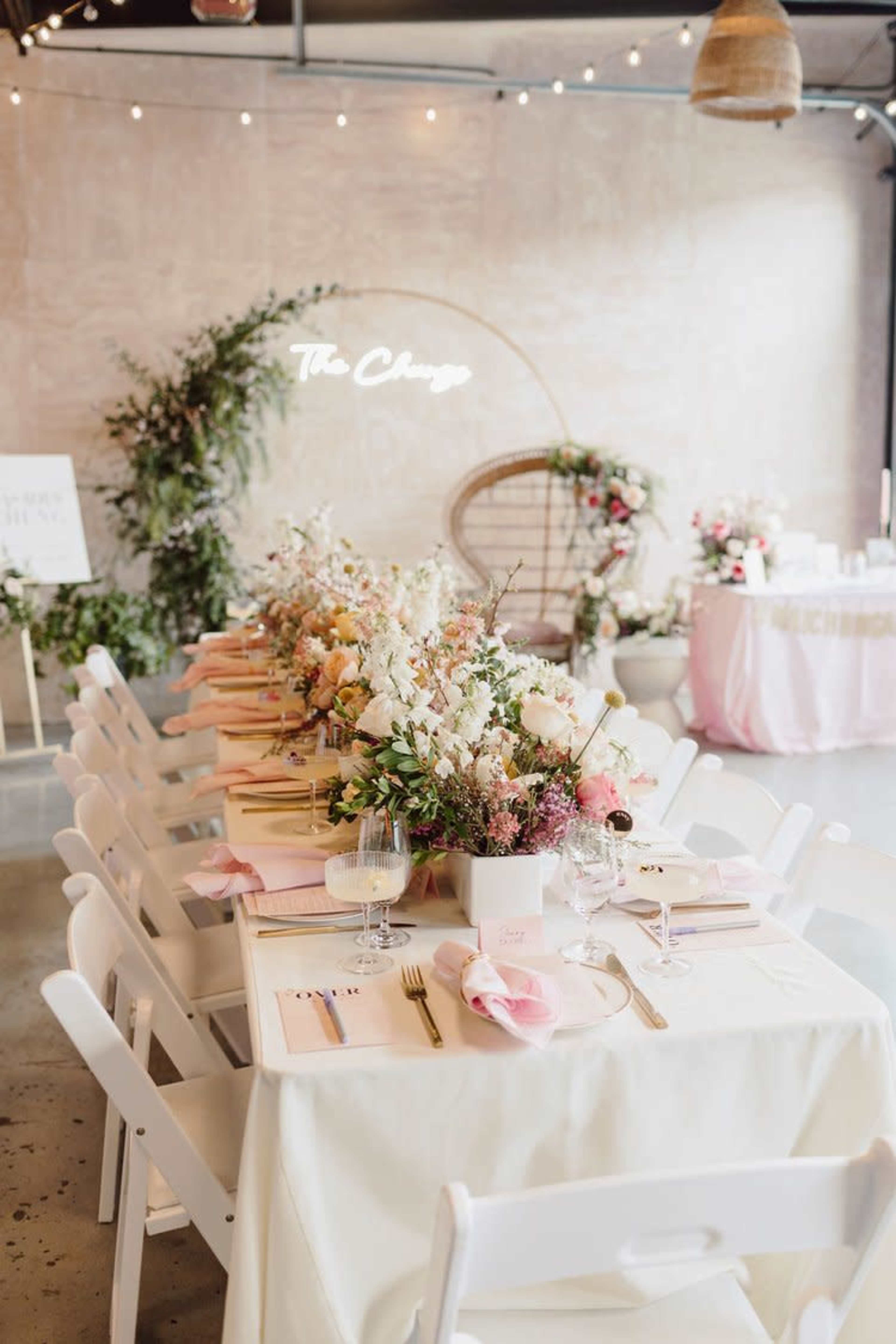 A long dining table is set with flowers and place settings, accompanied by a neon sign reading "The Change," in a decorated event space.