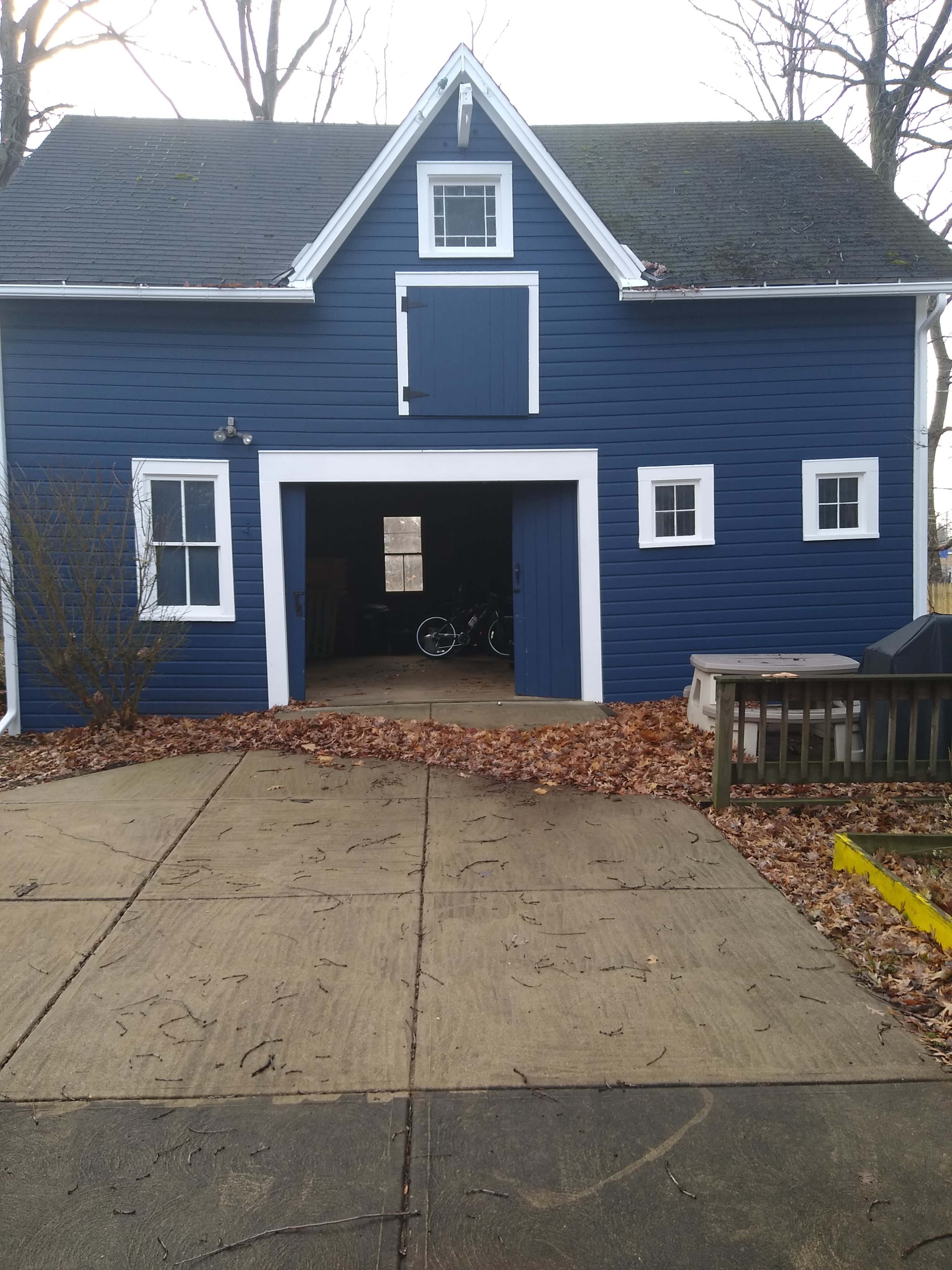 The image shows a blue barn-style garage with a large door, framed by trees and surrounded by fallen leaves.