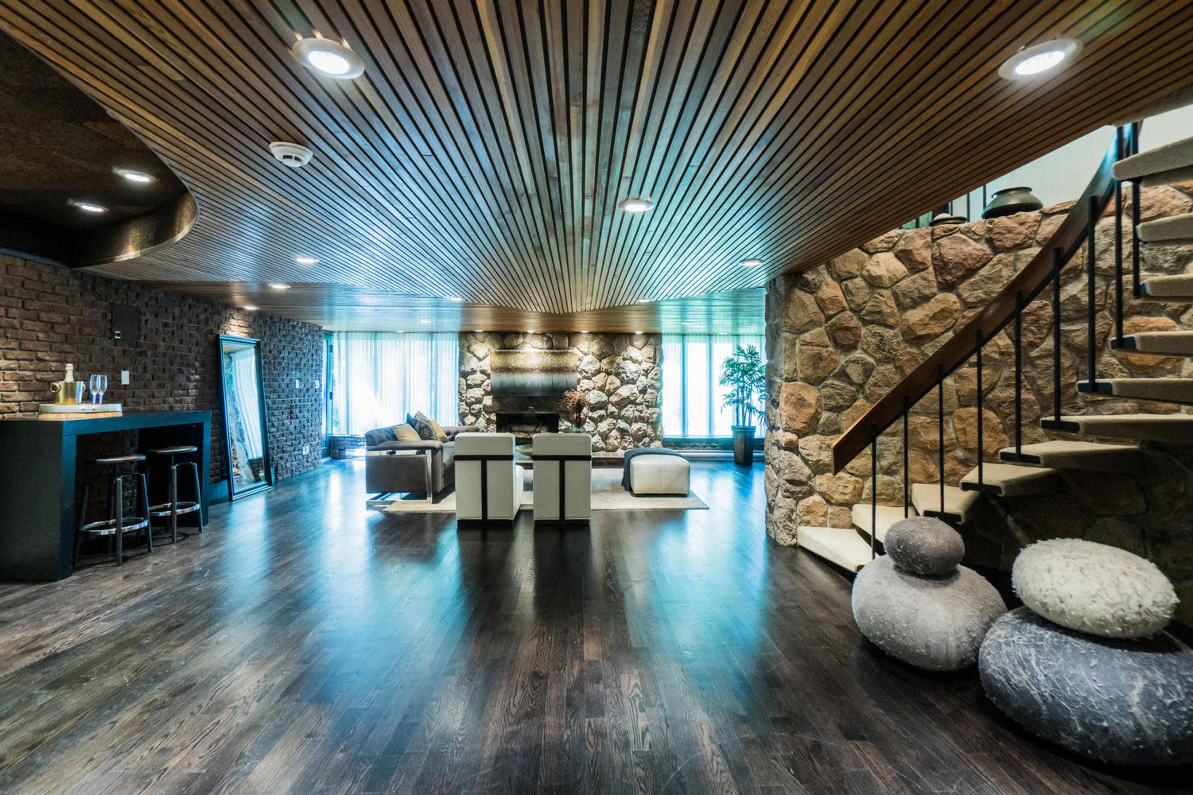 A spacious interior with a wooden ceiling, stone walls, and a staircase, featuring a seating area and a bar.