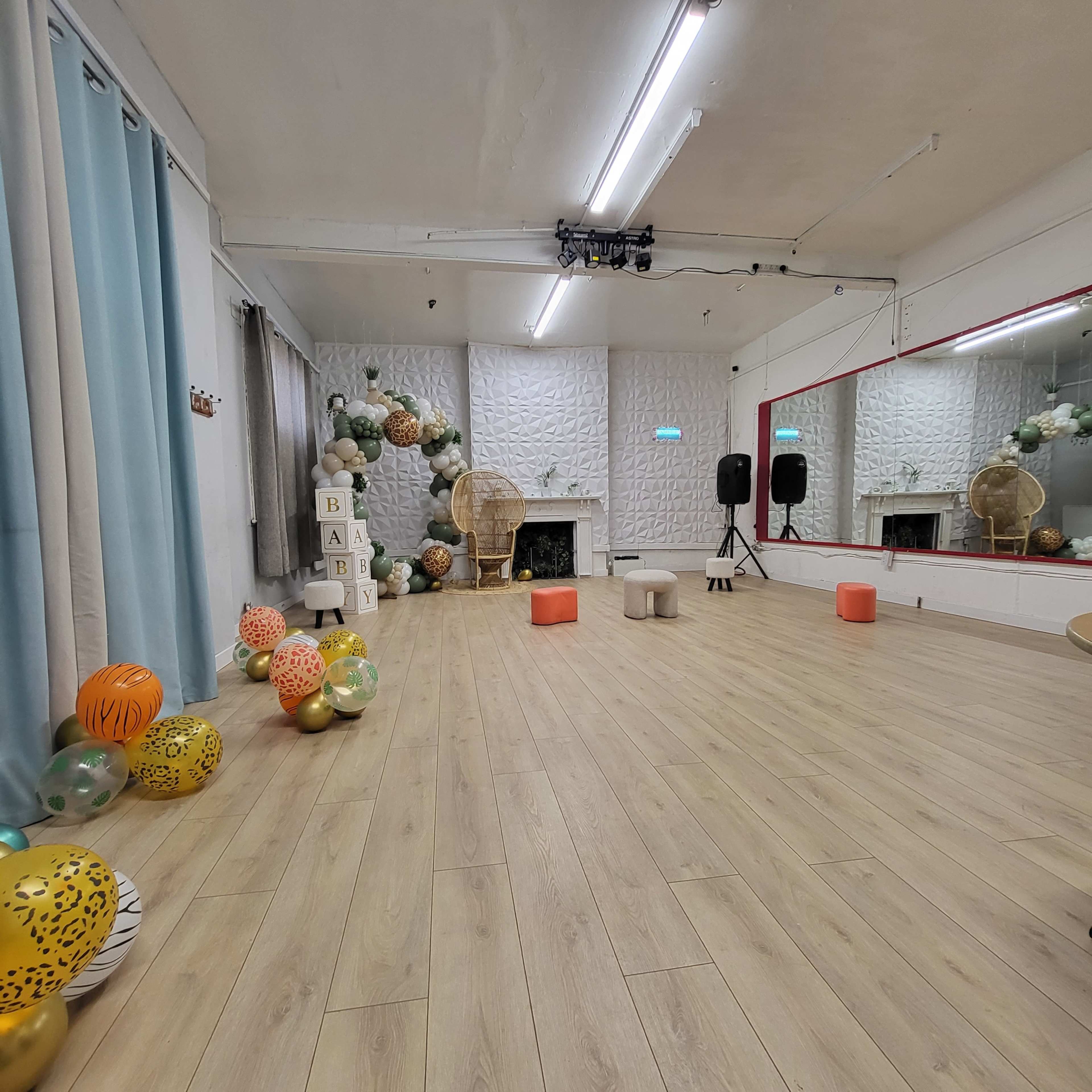 The image shows a spacious dance studio with light wooden flooring, decorated with colorful balloons and a mirrored wall.