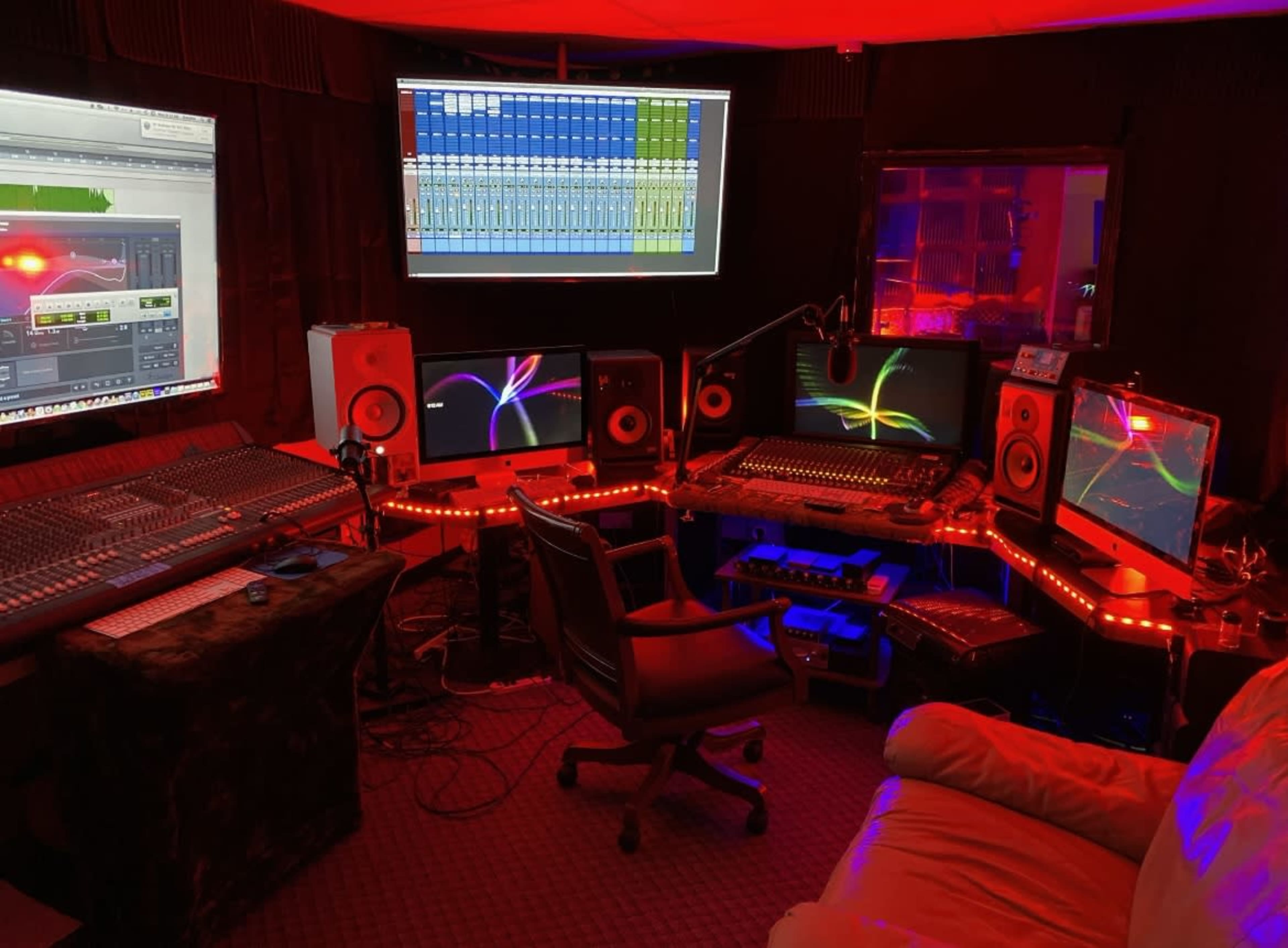 A music production studio filled with multiple computer monitors, mixing equipment, and LED lighting.
