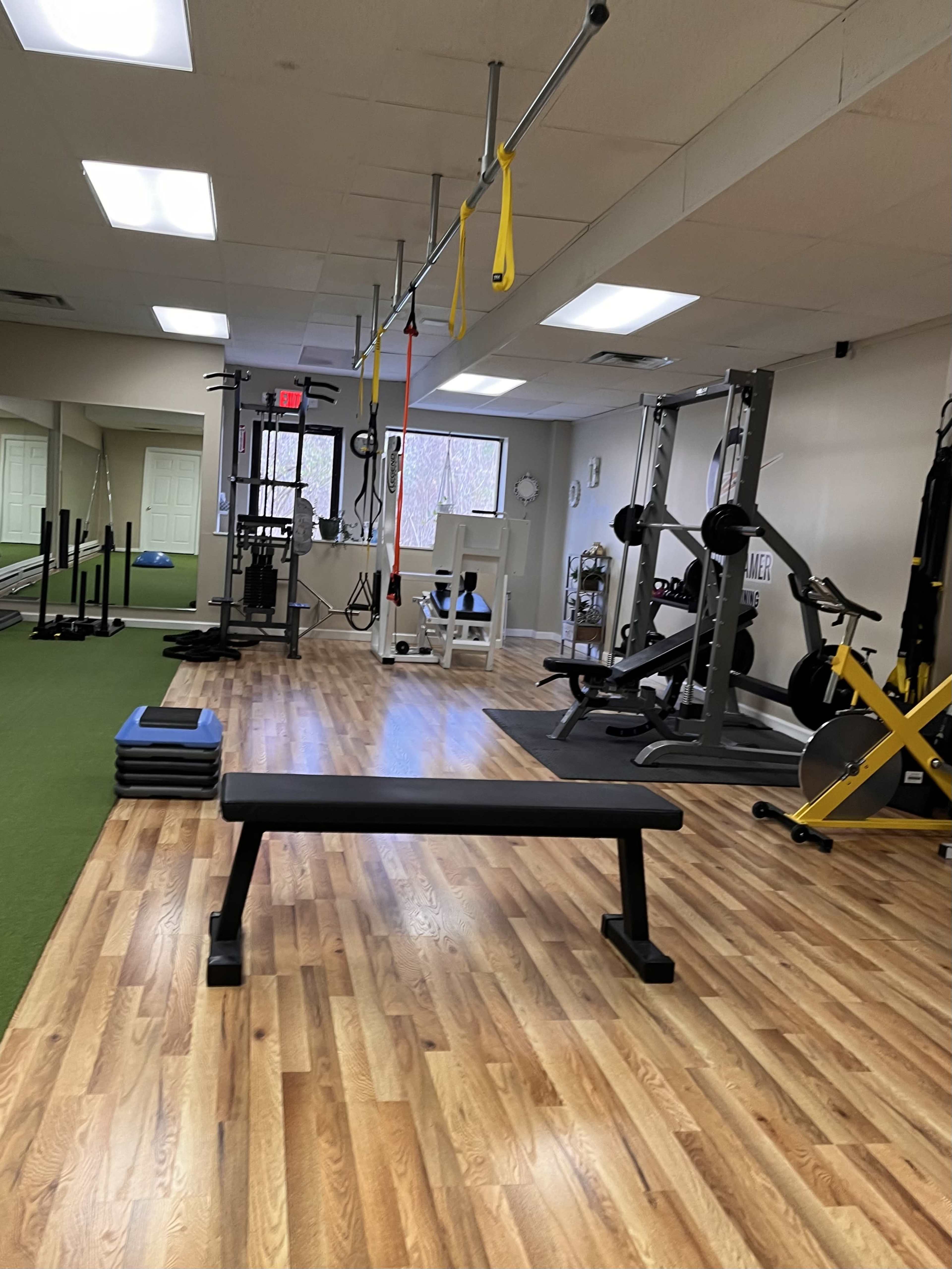 A gym interior with exercise equipment, a weight bench, and mats on a hardwood floor.