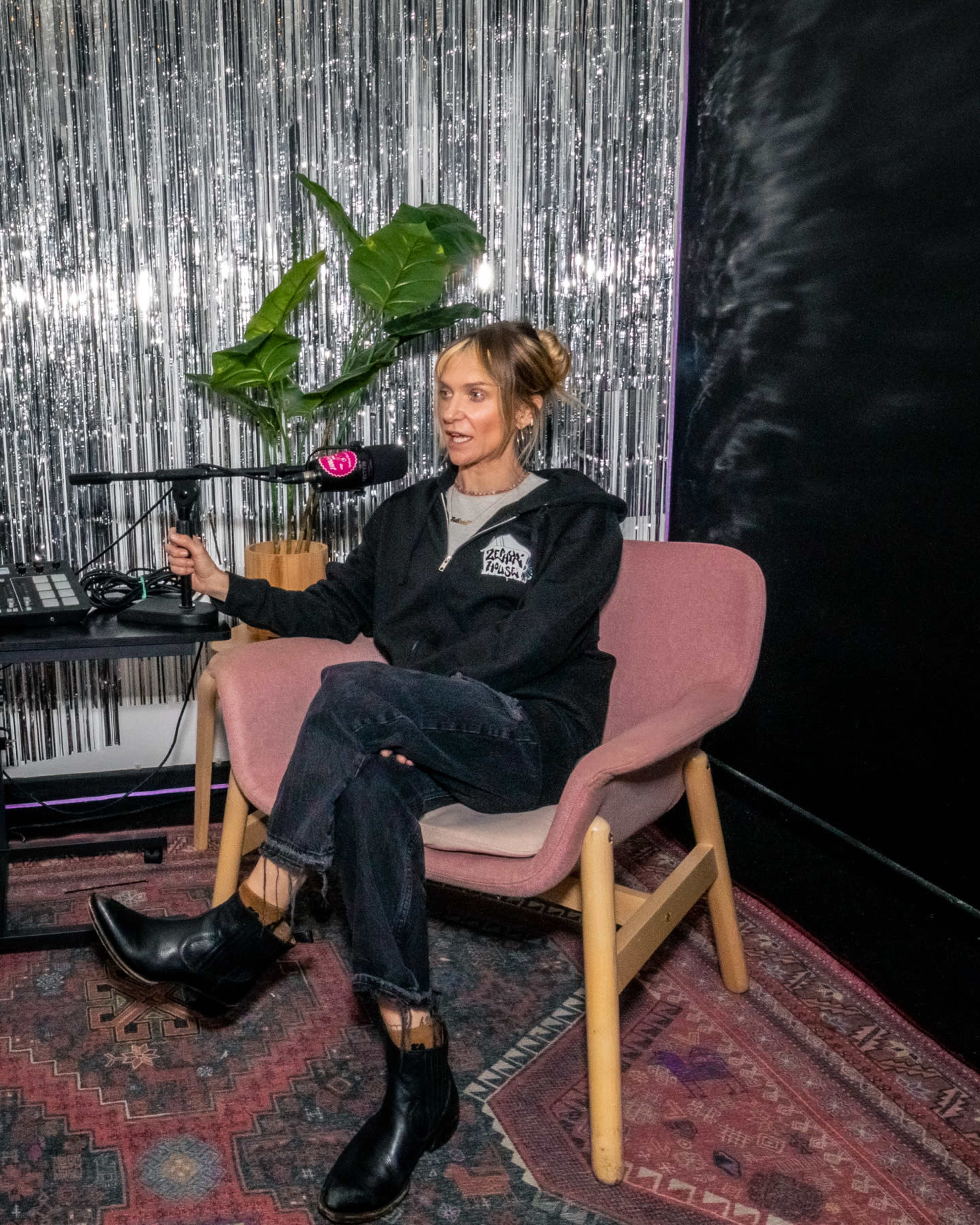 A person sits in a pink chair in front of a table with equipment, surrounded by shiny silver decorations and a green plant.