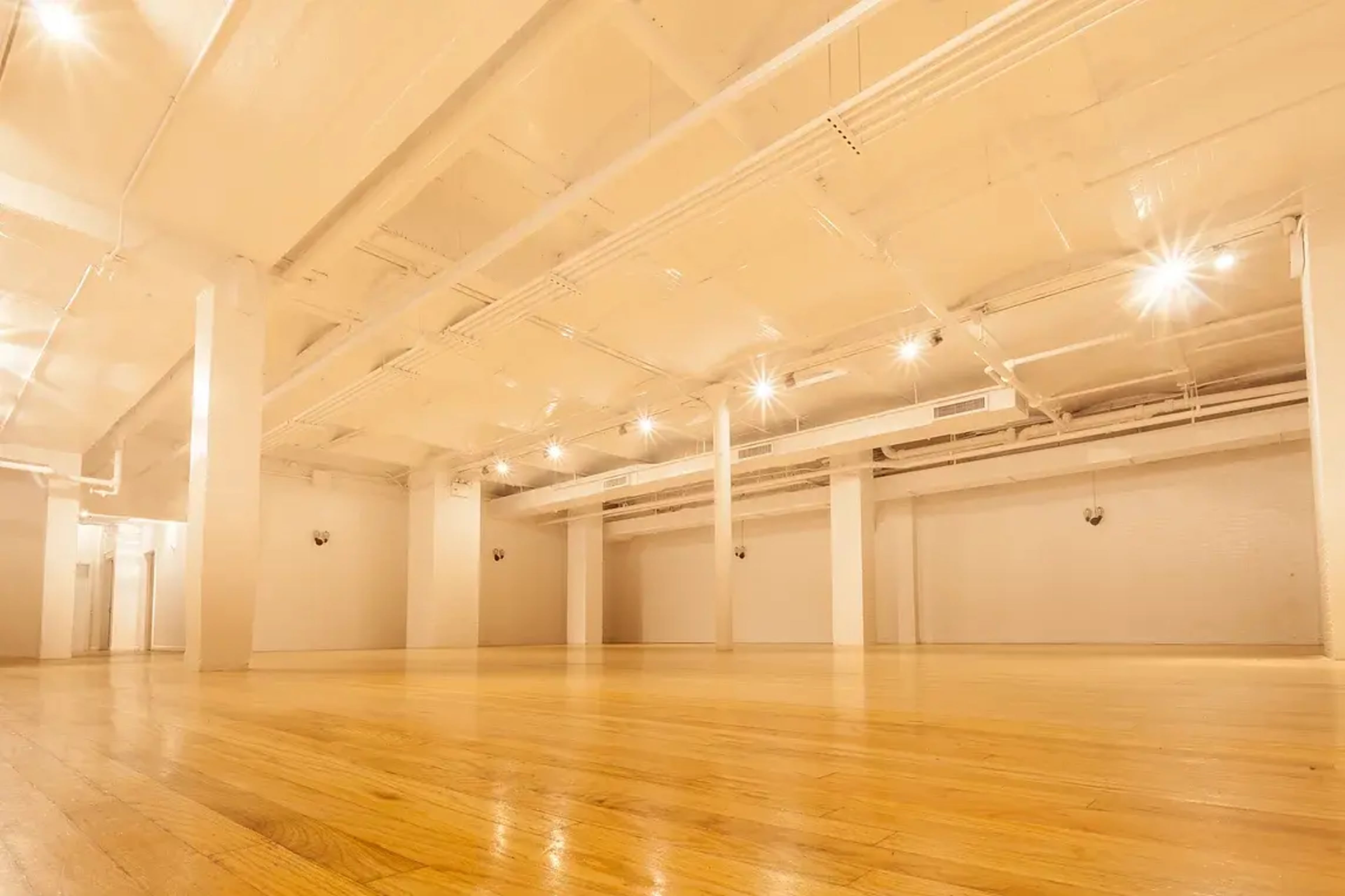 An empty, modern space with polished wooden floors and bright ceiling lights.