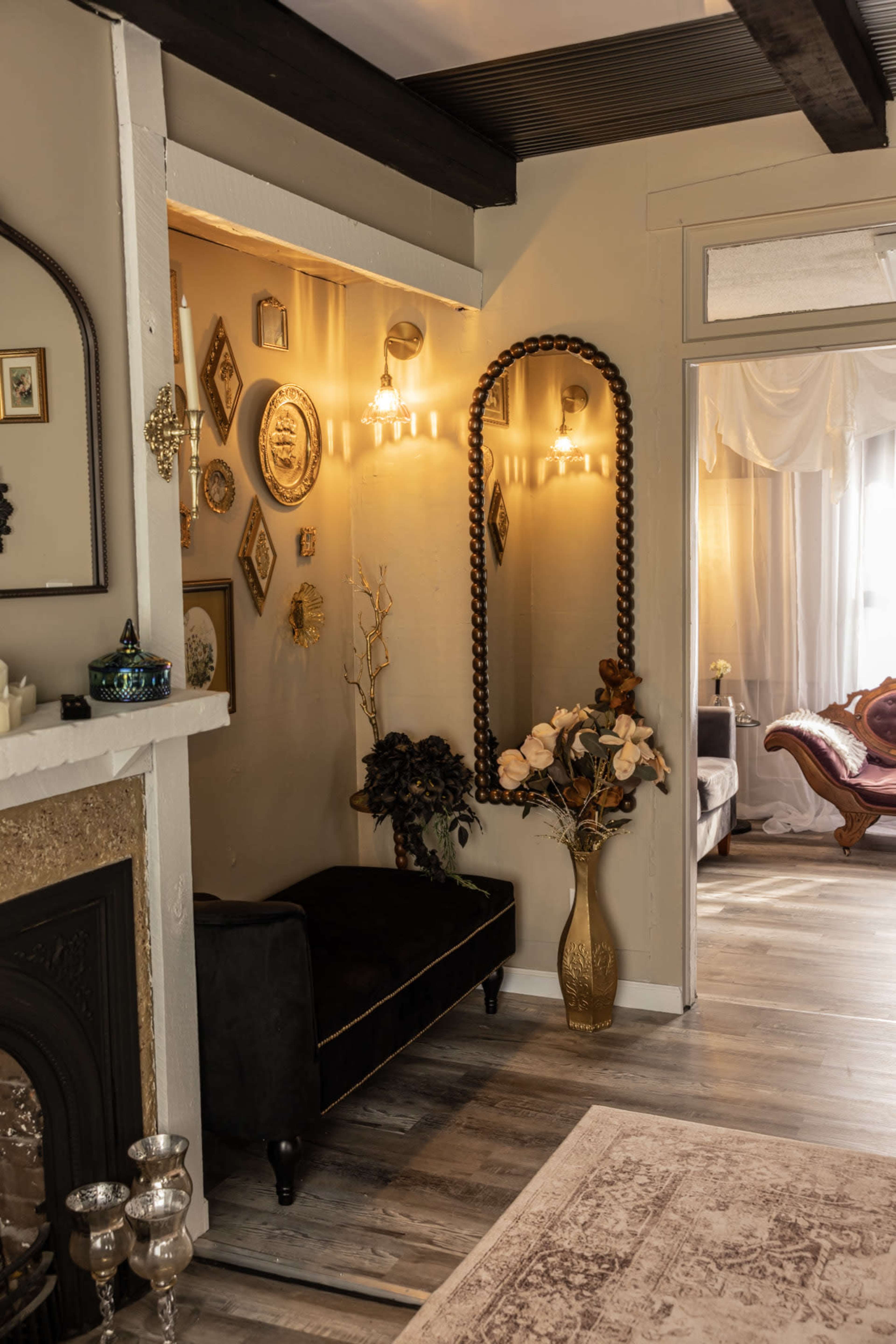 The image features a cozy interior with a decorative wall, a large mirror, and a floral arrangement next to a dimly lit corner of a room.