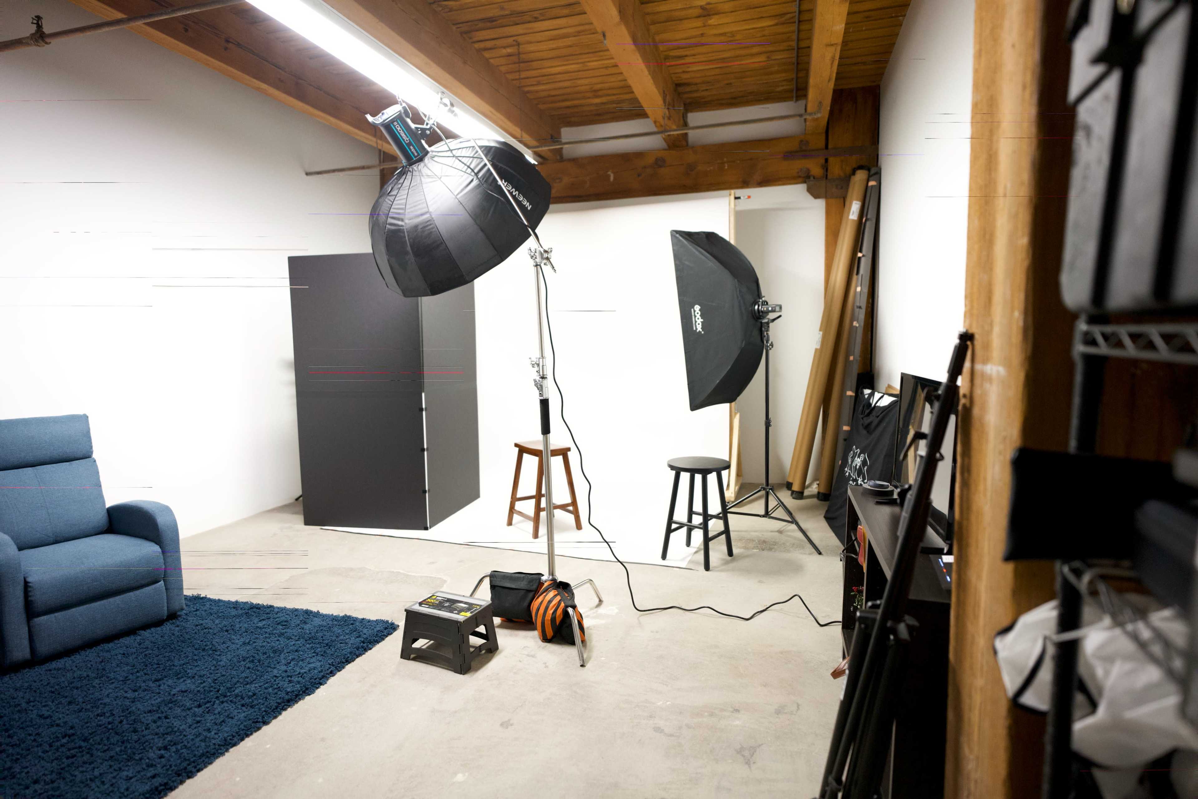 A photography studio with lighting equipment, a blue sofa, two stools, and various props on the floor.