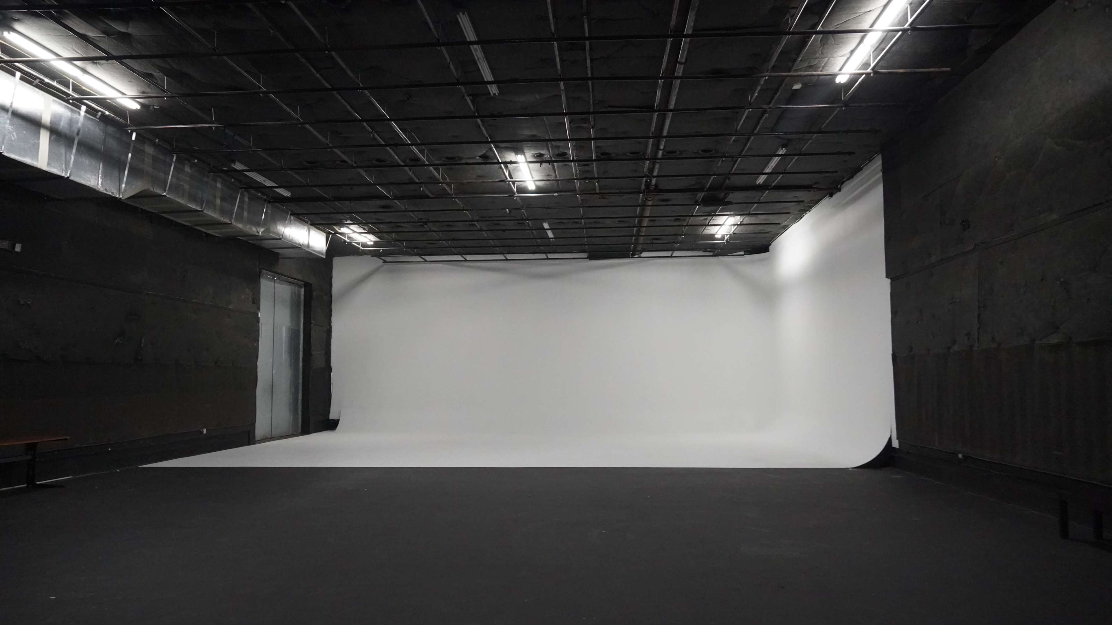 The image shows a large, empty studio with a white backdrop and dark flooring.