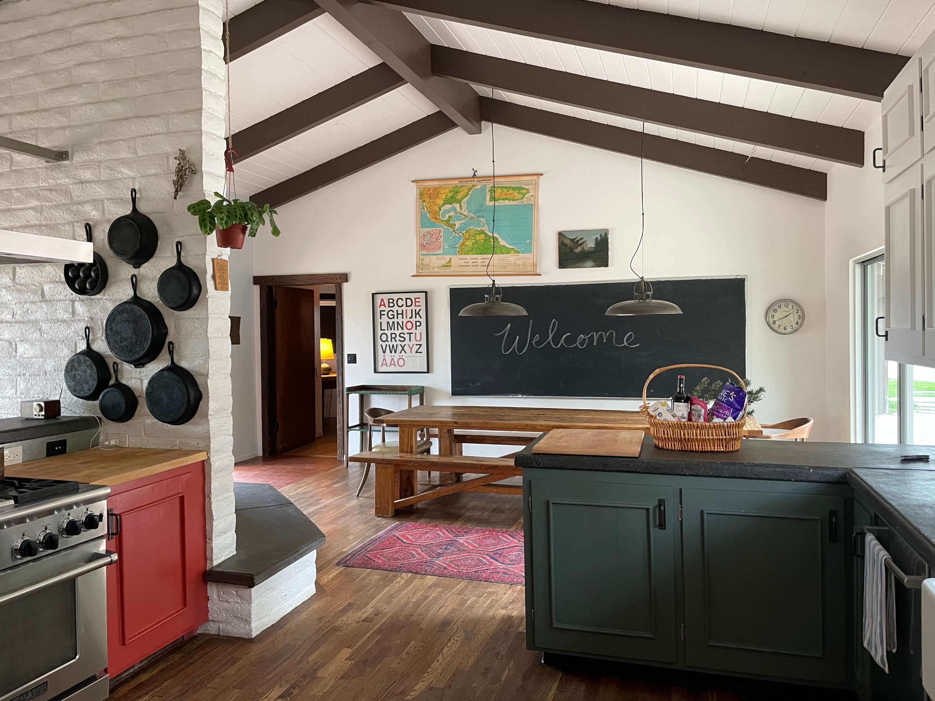 A spacious kitchen with a wooden dining table, chalkboard, wall-mounted pots, and an assortment of kitchen decor elements.