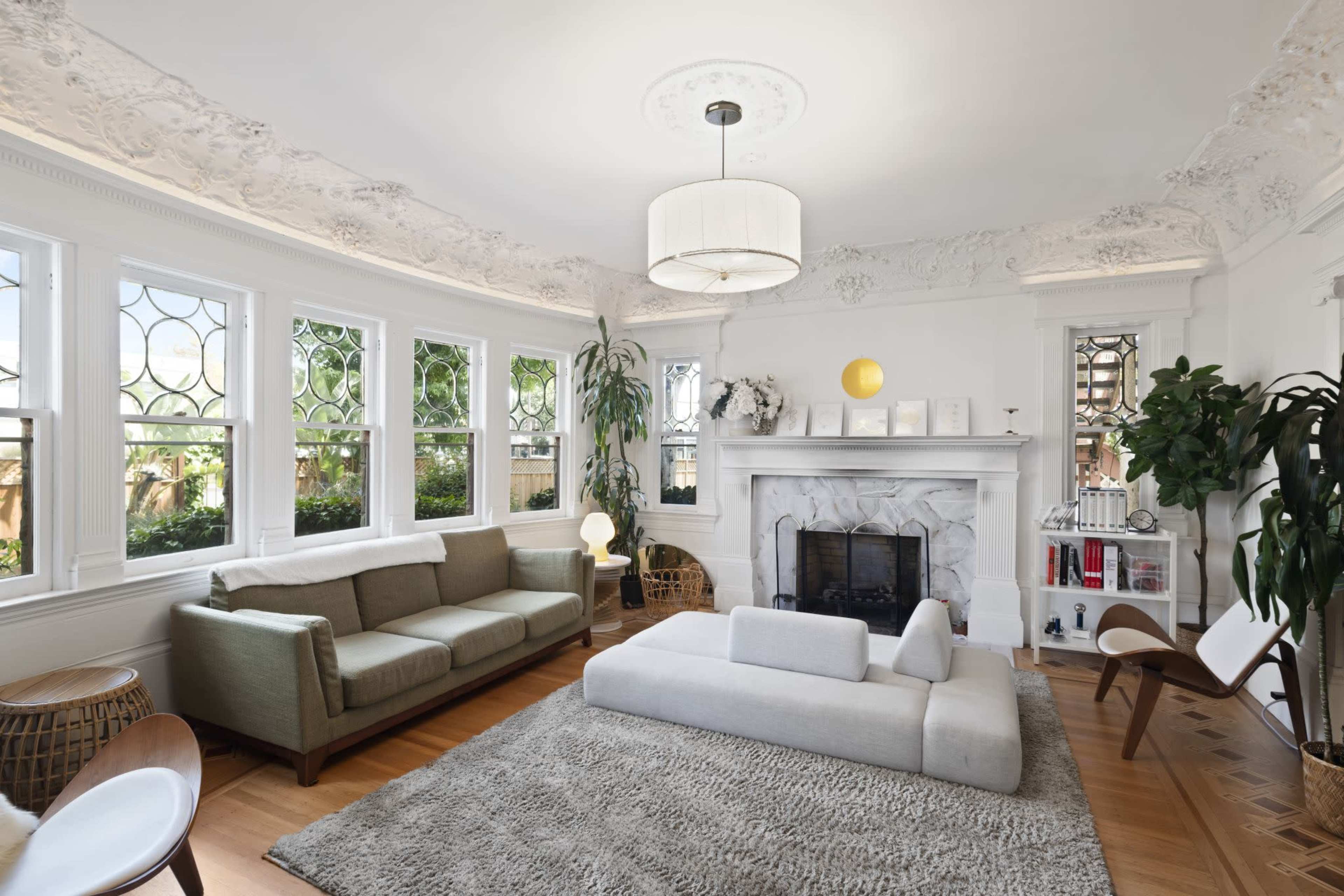 The image shows a well-lit living room featuring a large white couch, a green sofa, a fireplace with a stone facade, and decorative molding on the ceiling.