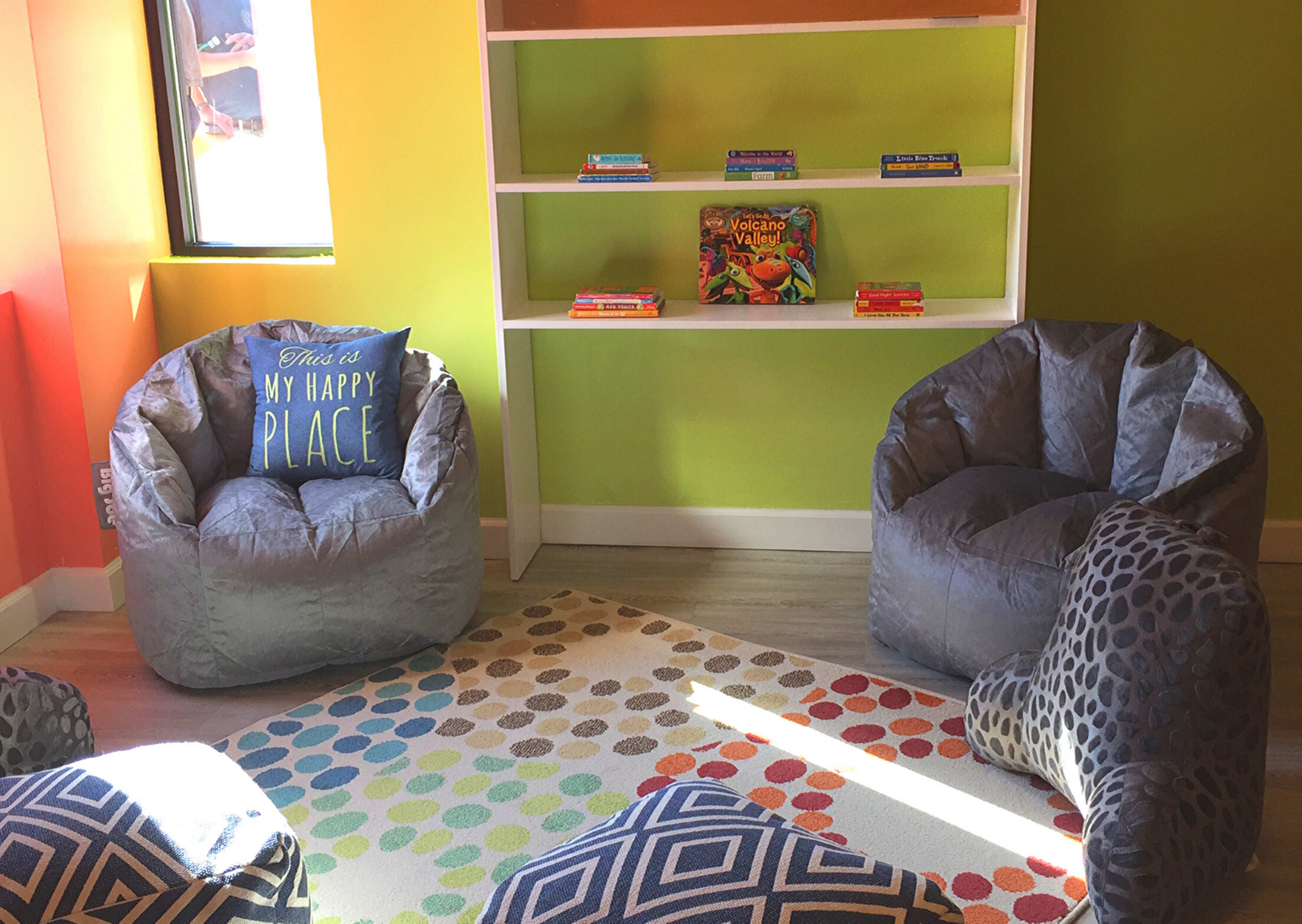 A brightly colored room with two bean bag chairs, a patterned rug, and a shelf filled with books.