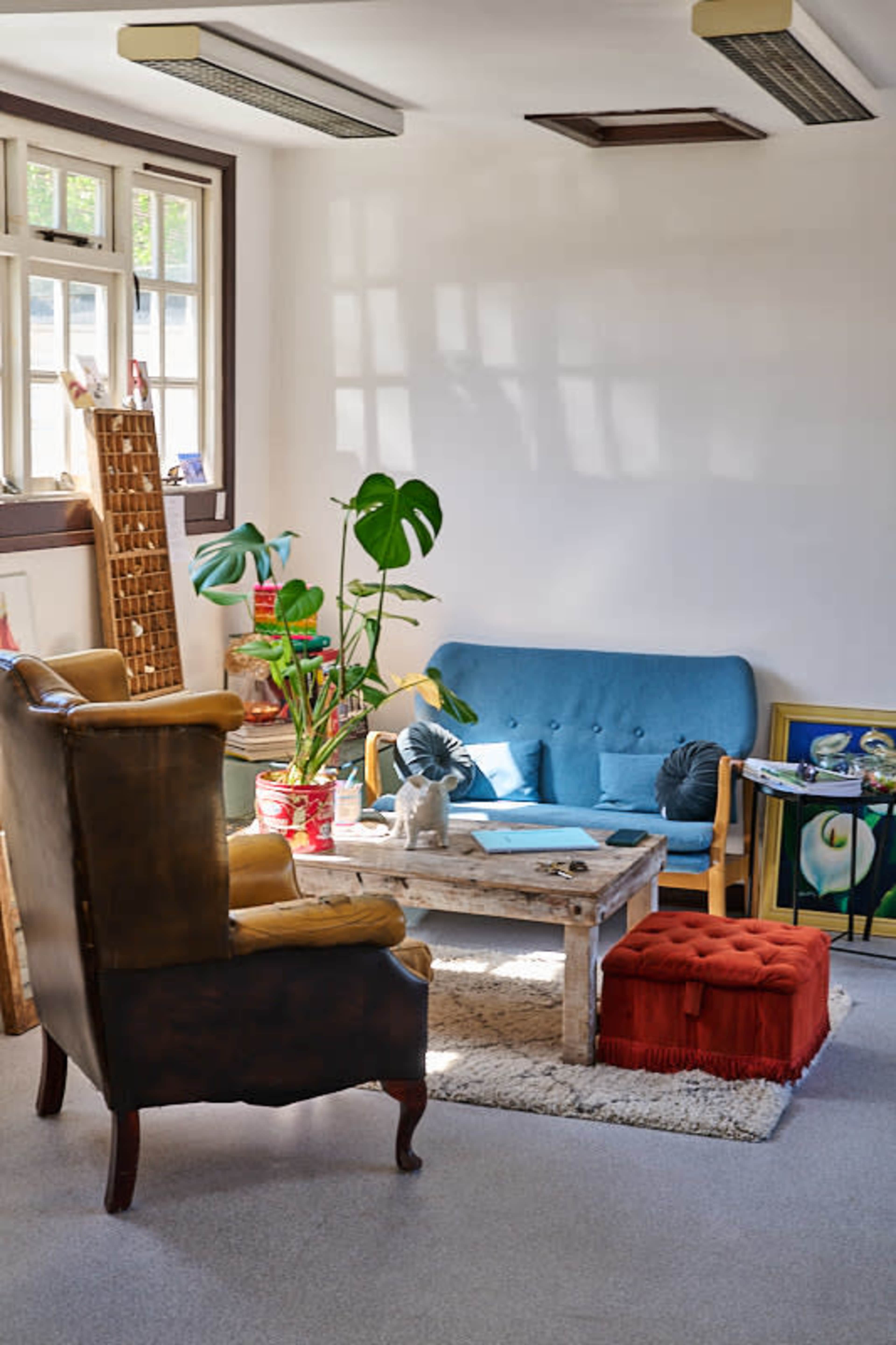 The image shows a cozy living room featuring a blue sofa, an armchair, a coffee table, and various decorative items, with sunlight streaming through the windows.