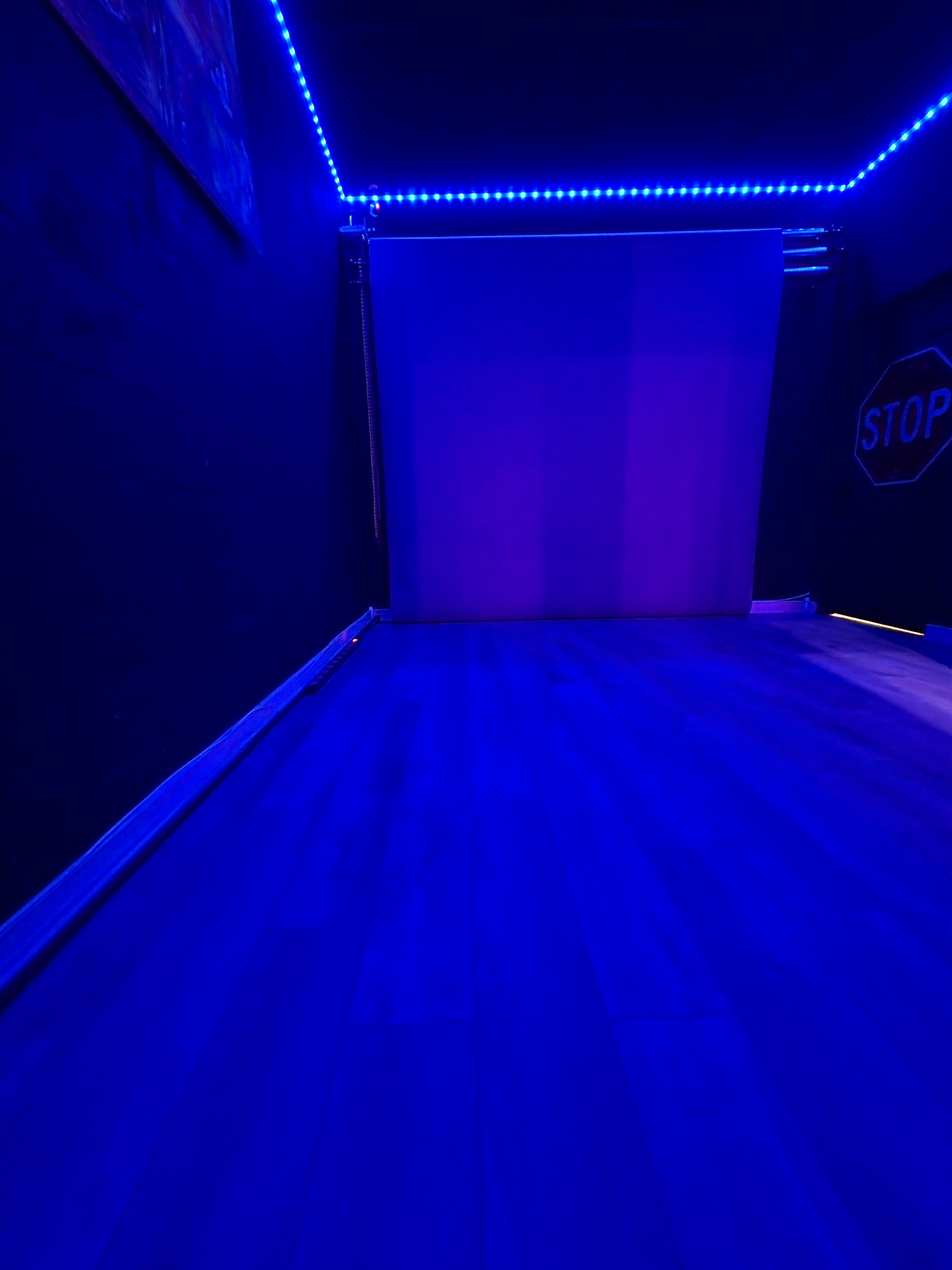 The image shows a dimly lit room with blue LED lights illuminating the walls and a blank white backdrop at the far end.