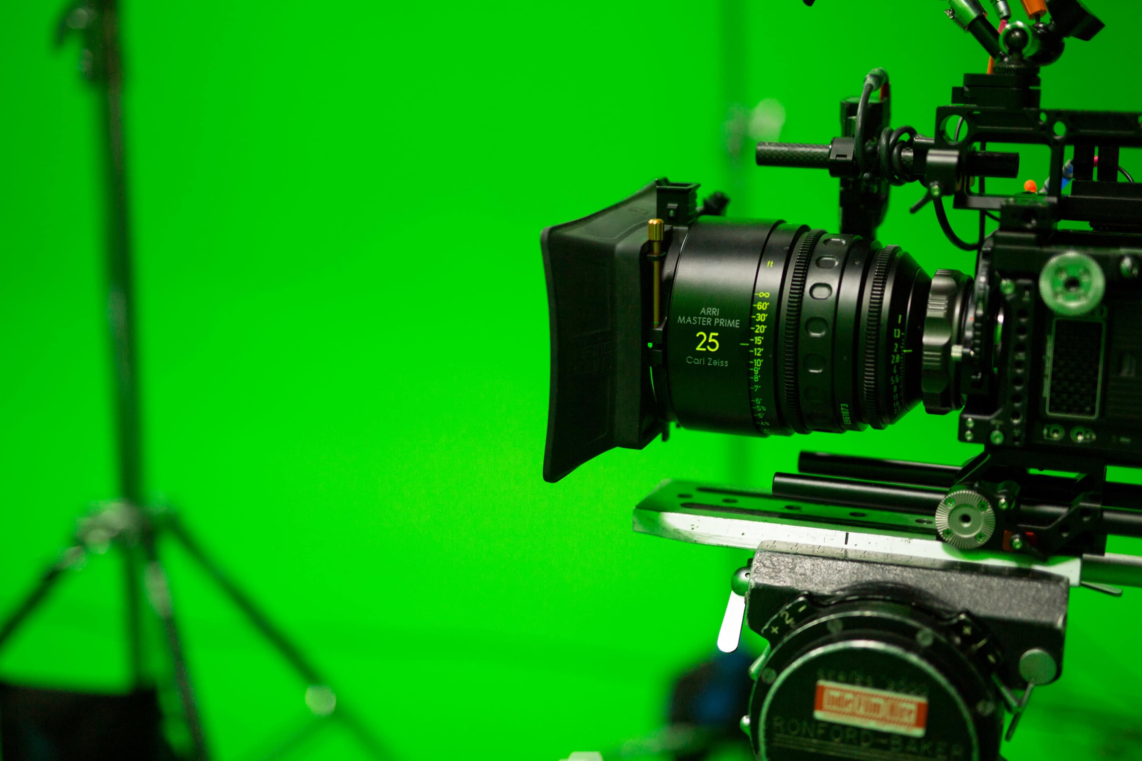 A professional camera lens is focused on a bright green backdrop in a film production setup.