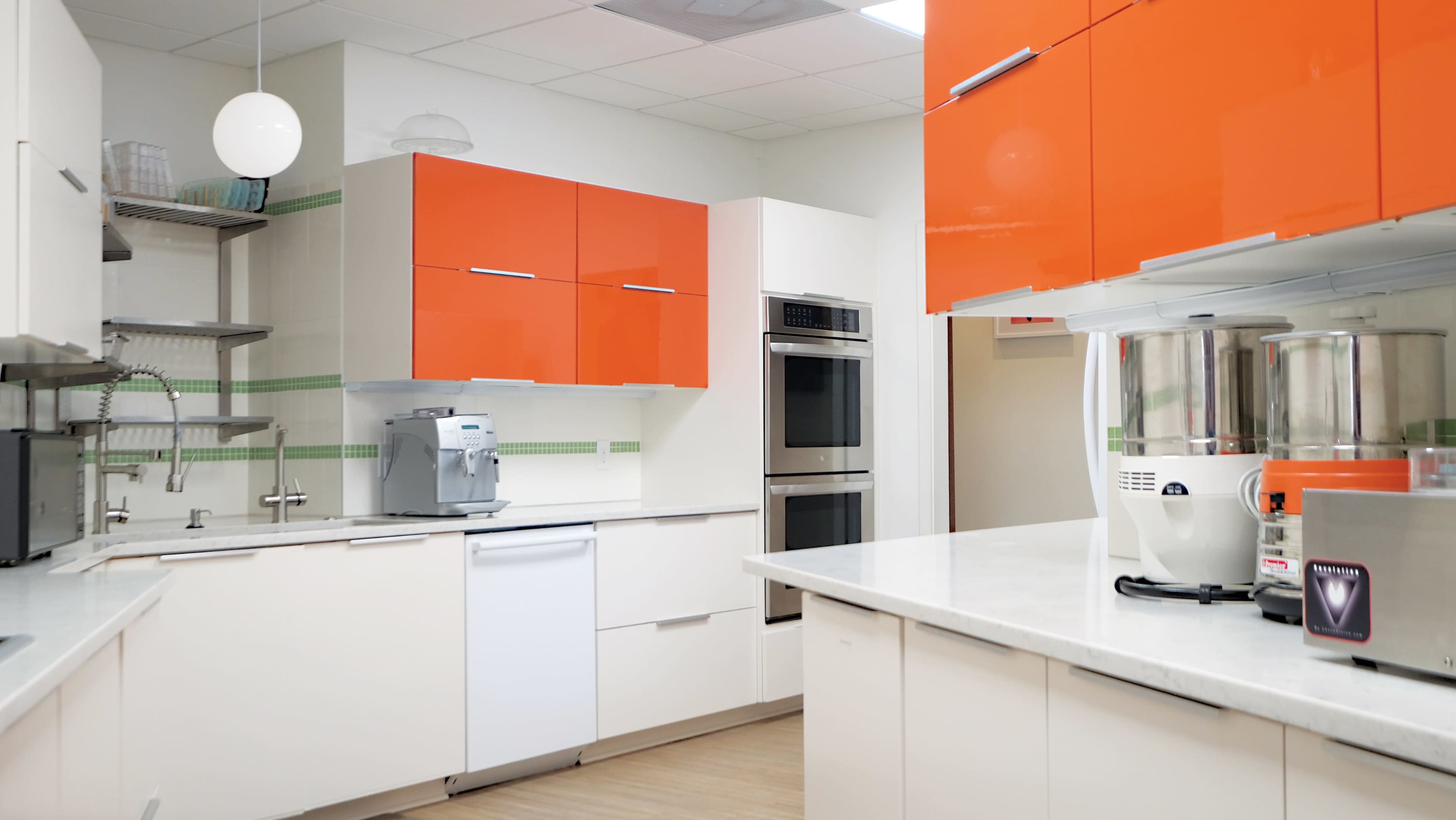 A modern kitchen features orange upper cabinets, stainless steel appliances, and a smooth white countertop.