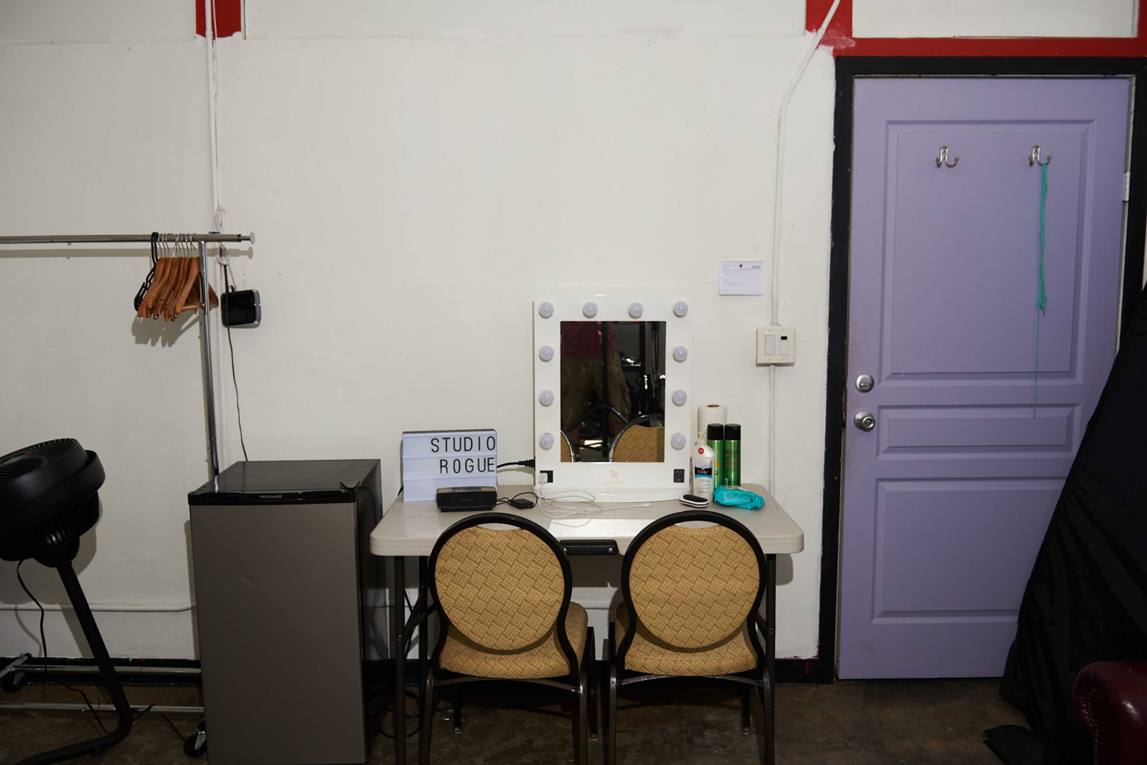 A small dressing area features a table with a lighted mirror, two chairs, and a purple door in the background.