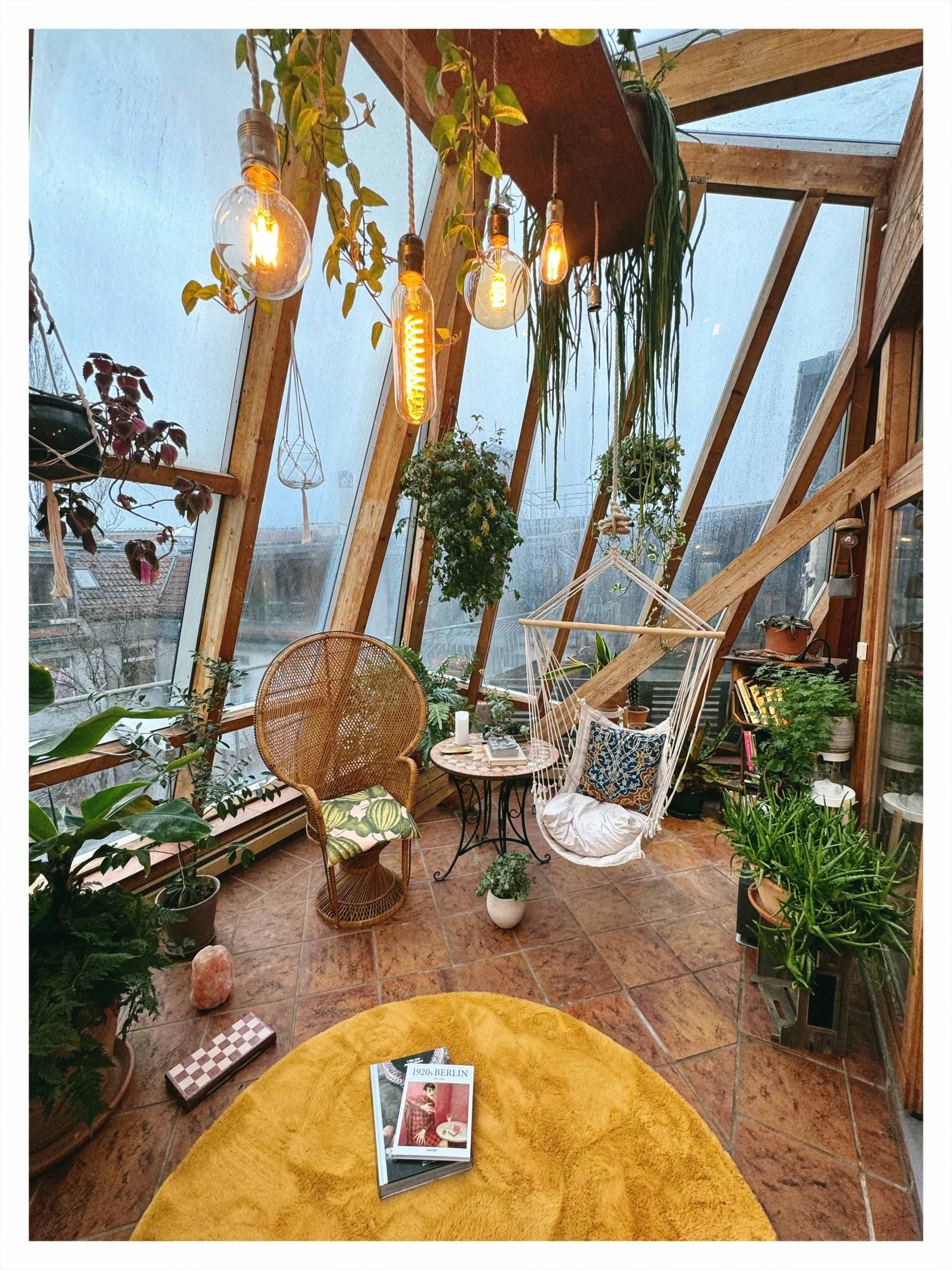 The image shows a cozy, plant-filled sunroom with a hanging chair, warm lighting, and a round rug, creating an inviting atmosphere.