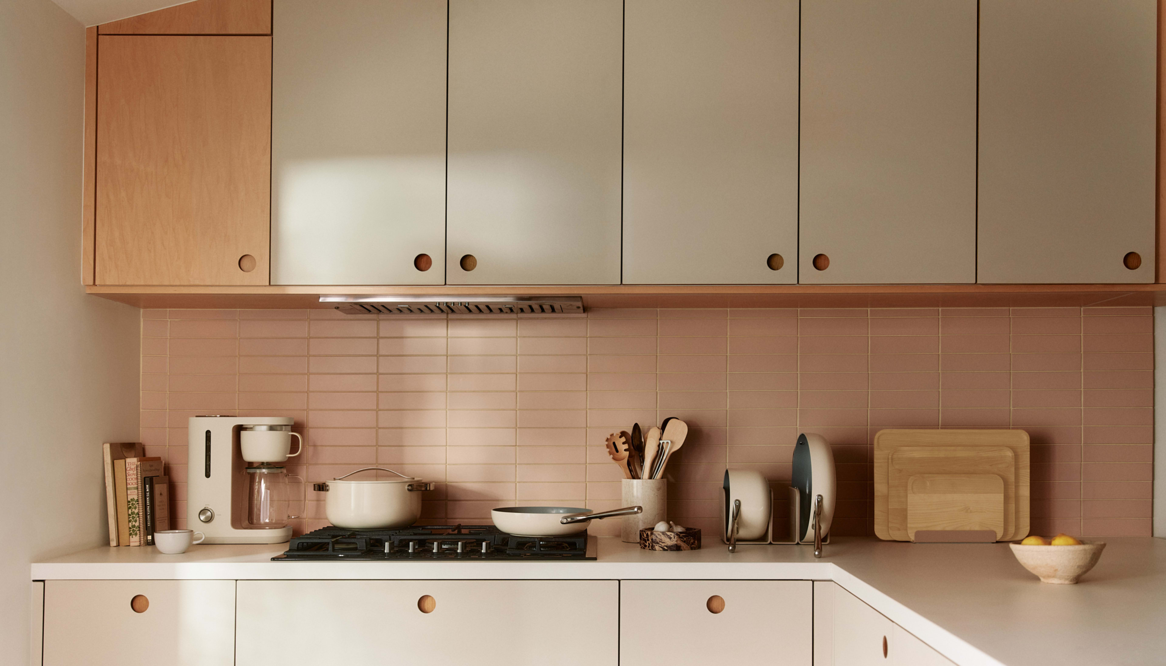 A modern kitchen features light-colored cabinets, a stovetop, and various cooking utensils arranged on the counter.
